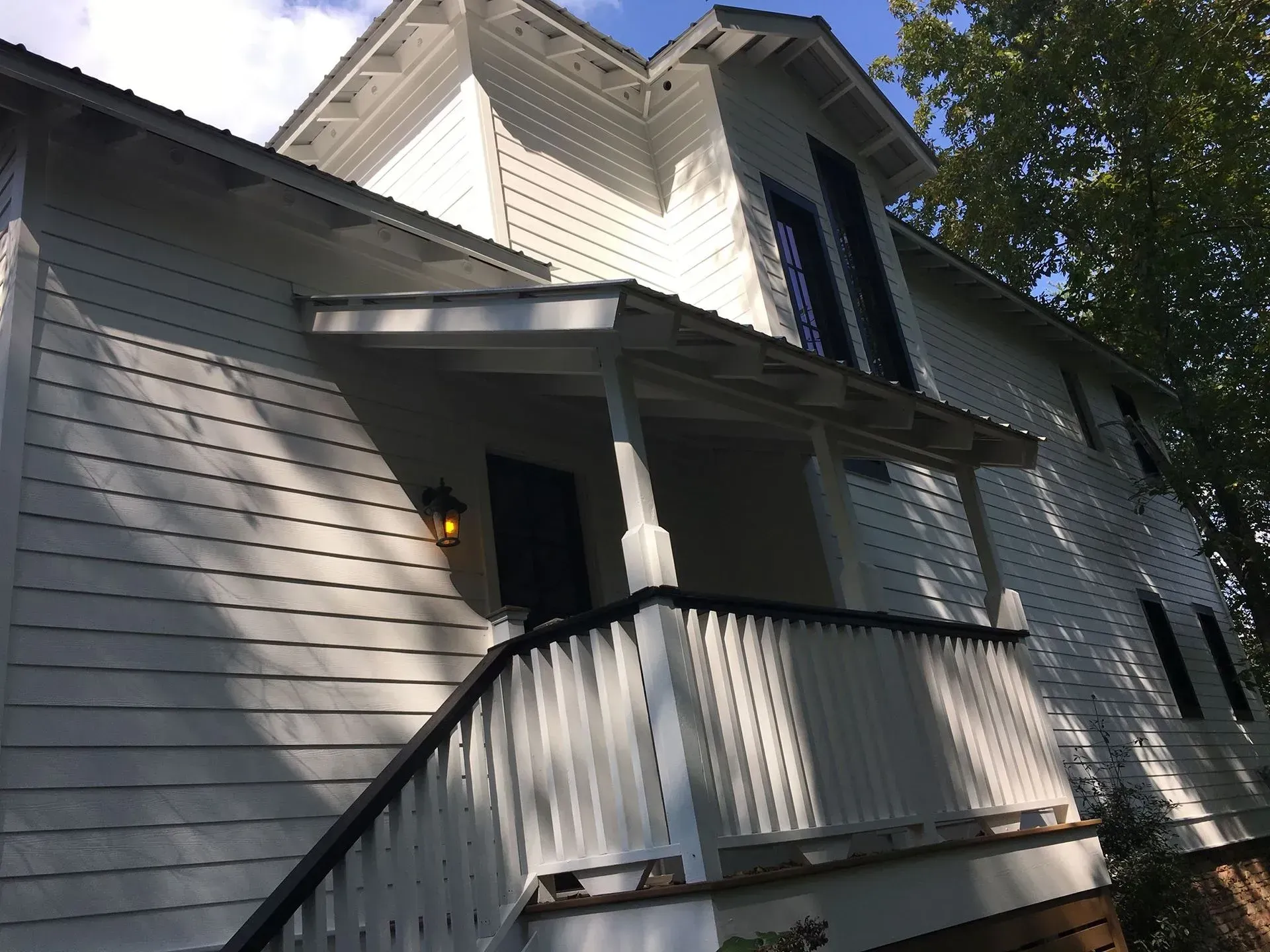 White, two-story house with a porch. Black railings and trim contrast against the white siding. Sunlight casts shadows.