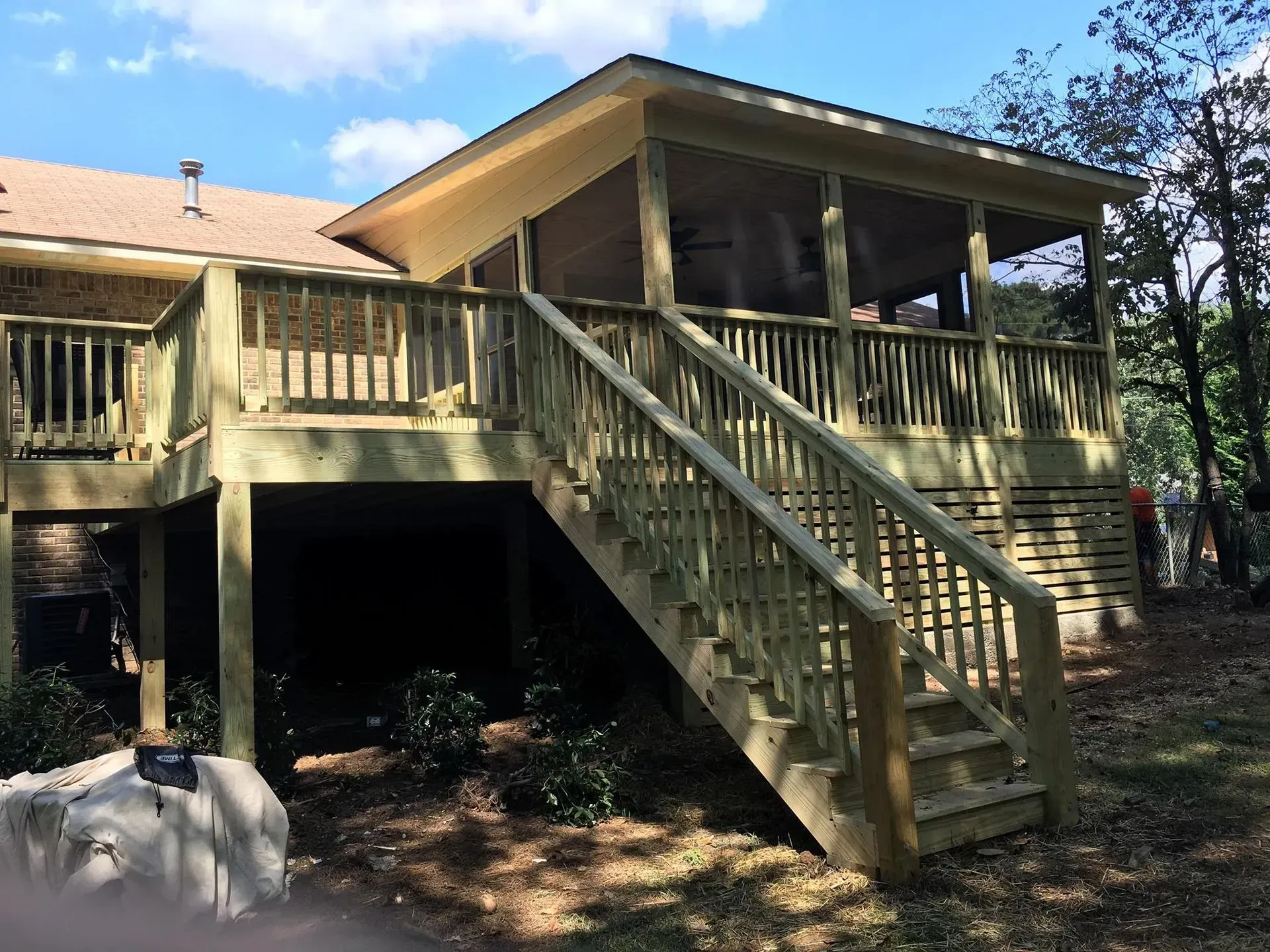 Wooden deck and screened porch extension on the back of a house with a set of stairs leading down to a yard.