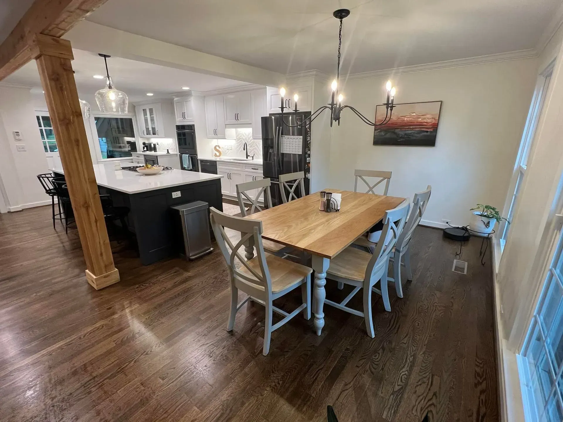 Dining room with wooden table and chairs, leading to an open kitchen. Hardwood floors, white cabinets, and black island.