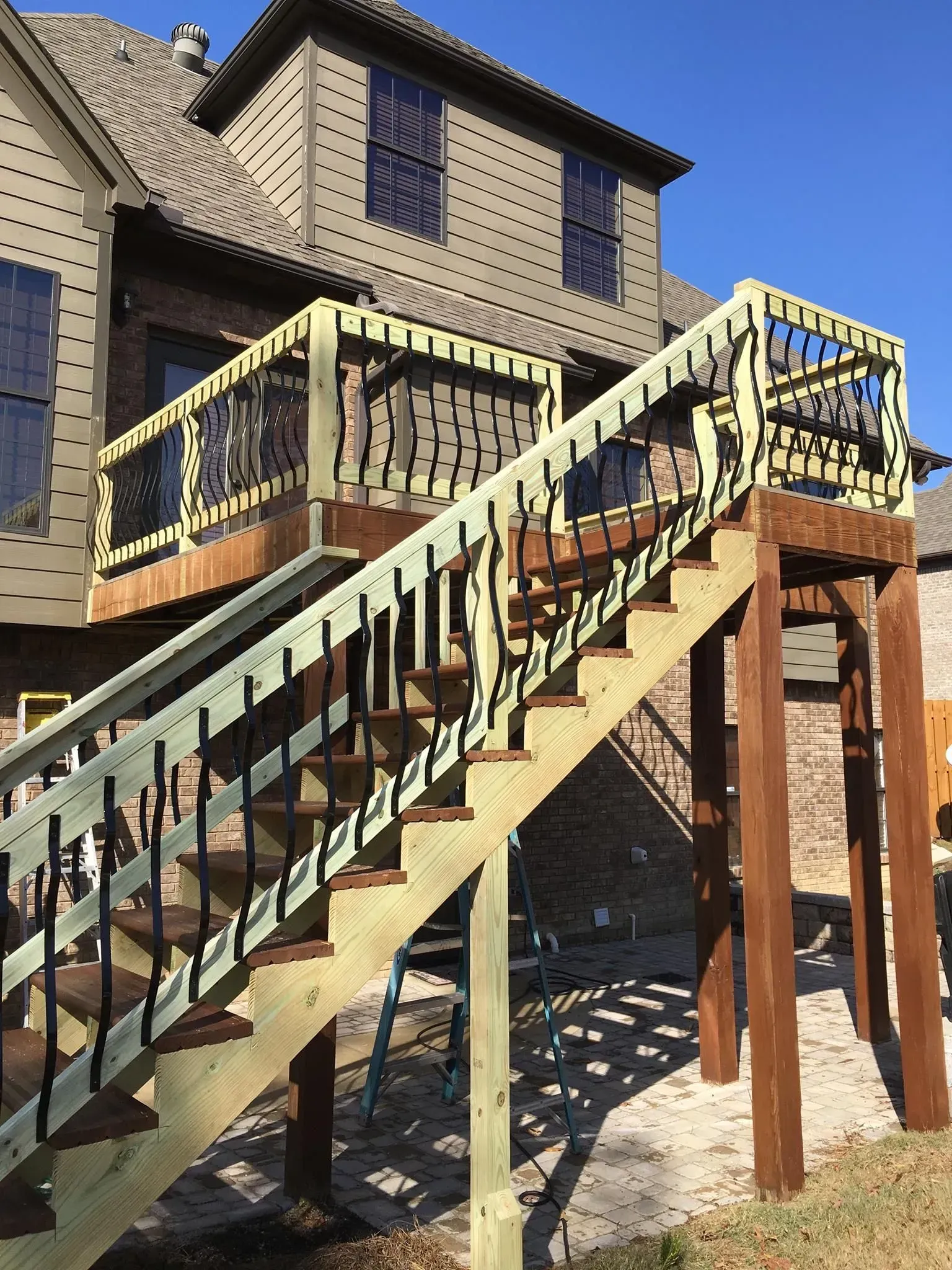 A two-story deck with stairs, painted light green and brown, on the back of a brick house.