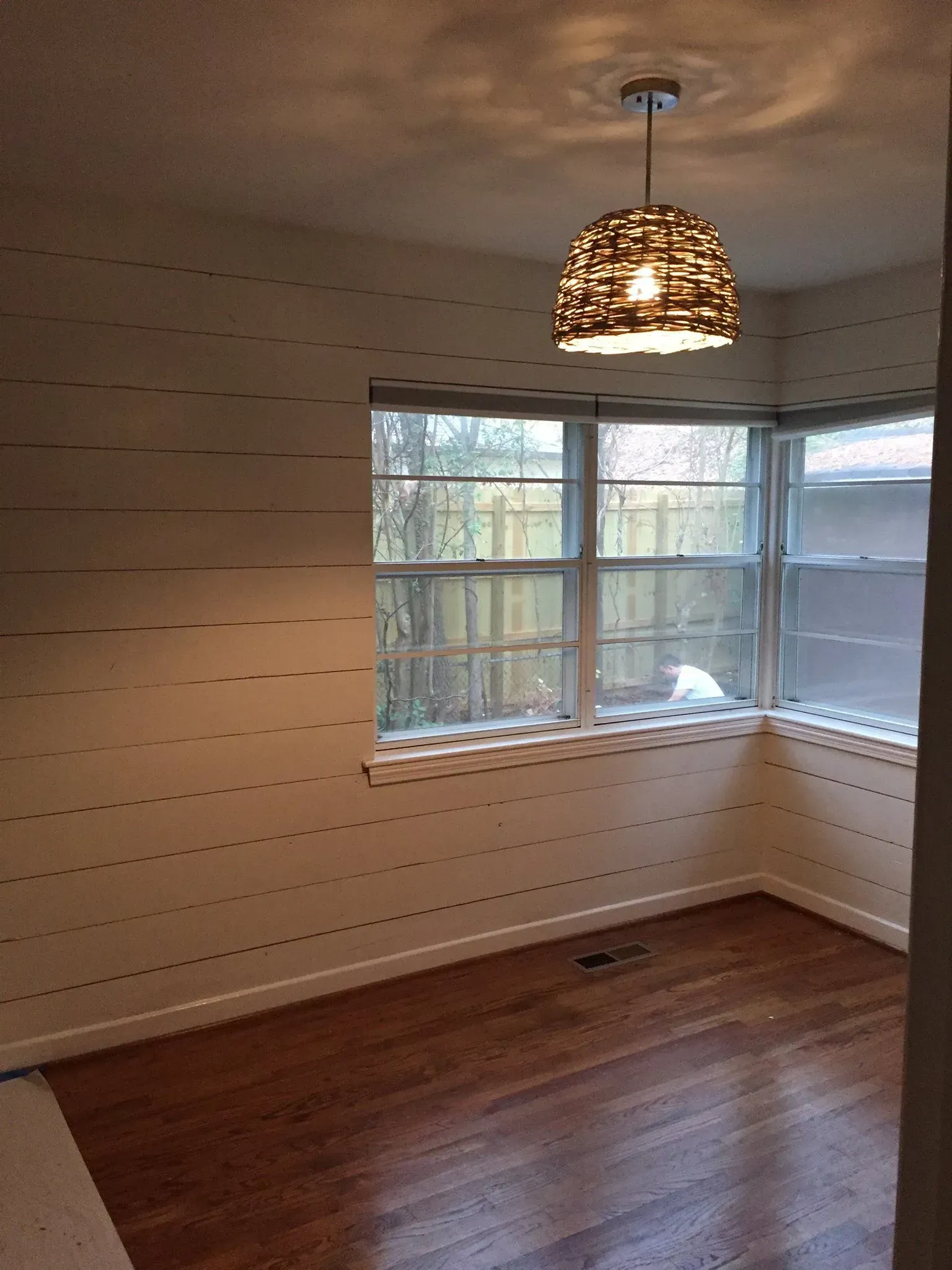 A bright, empty room with a patterned lampshade, windows, and hardwood floors.