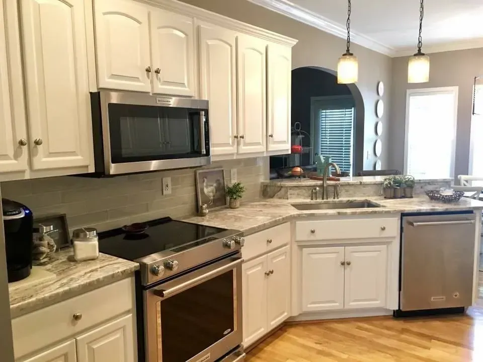 White kitchen with stainless steel appliances, light countertops, and white cabinets. Hardwood floor.