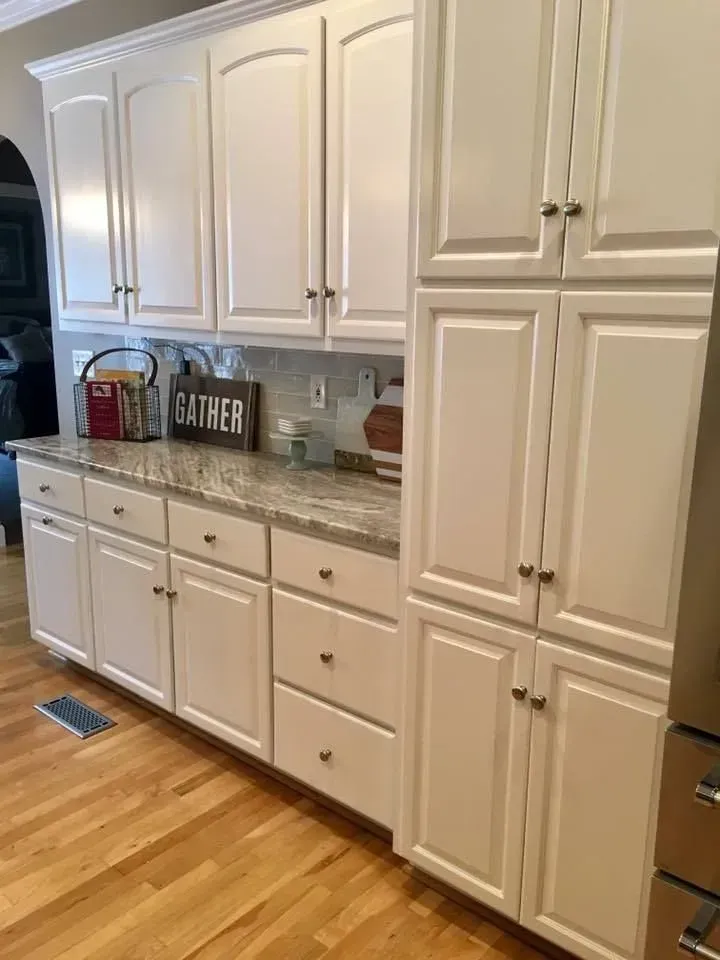 White kitchen cabinets with granite countertops and hardwood floors. A 