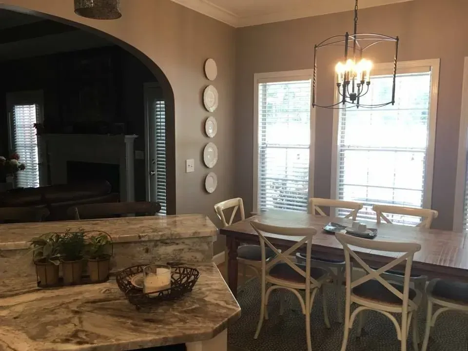 A dining room with a table and chairs, next to a kitchen island with a stone countertop.