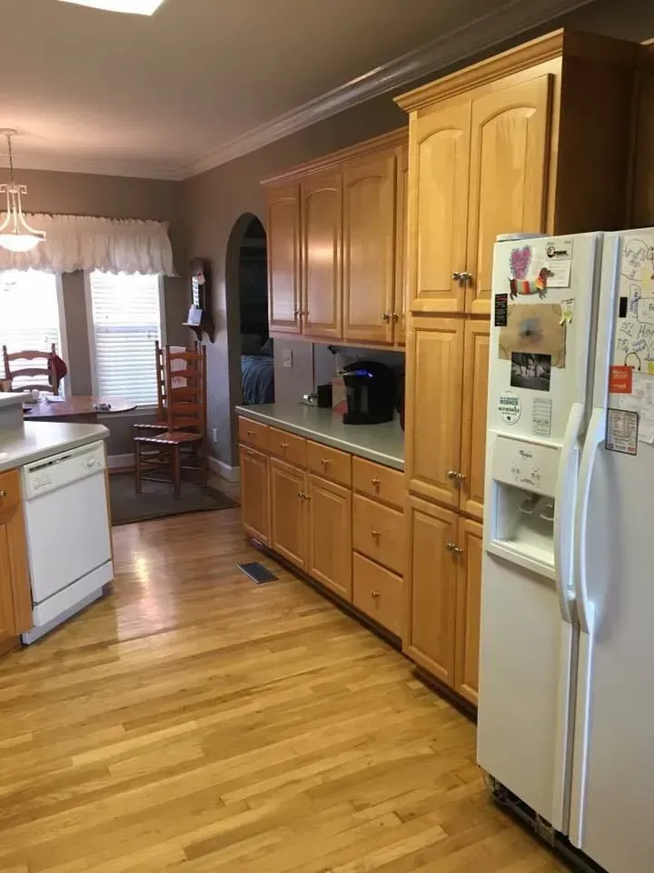 A kitchen with wooden cabinets, hardwood floors, and white appliances. A refrigerator stands next to tall cabinets