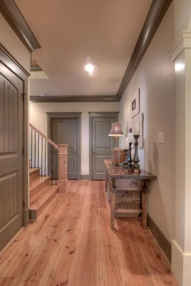 Hallway with wooden floors, stairs, and a rustic table with a lamp and decor. 