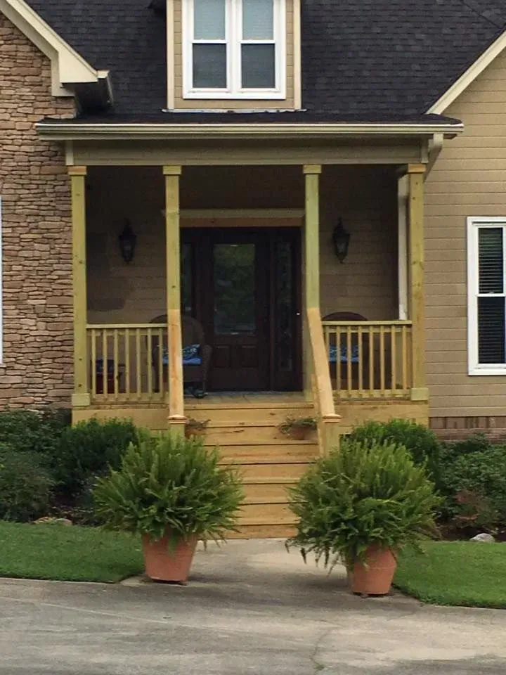 Front of a beige house with a porch. Two potted plants flank the front steps.