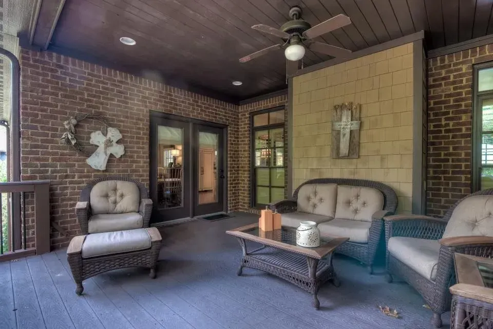 A covered porch with wicker furniture, brick walls, and a wooden ceiling.
