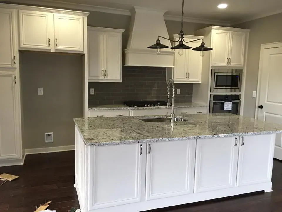 White kitchen with island, granite countertops, and stainless steel appliances. Cabinets and dark wood flooring.