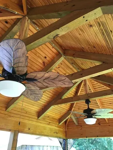 View of a wooden gazebo ceiling with two leaf-shaped ceiling fans.