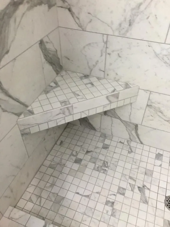 Shower corner with a triangular built-in seat and marble tile walls and floor.