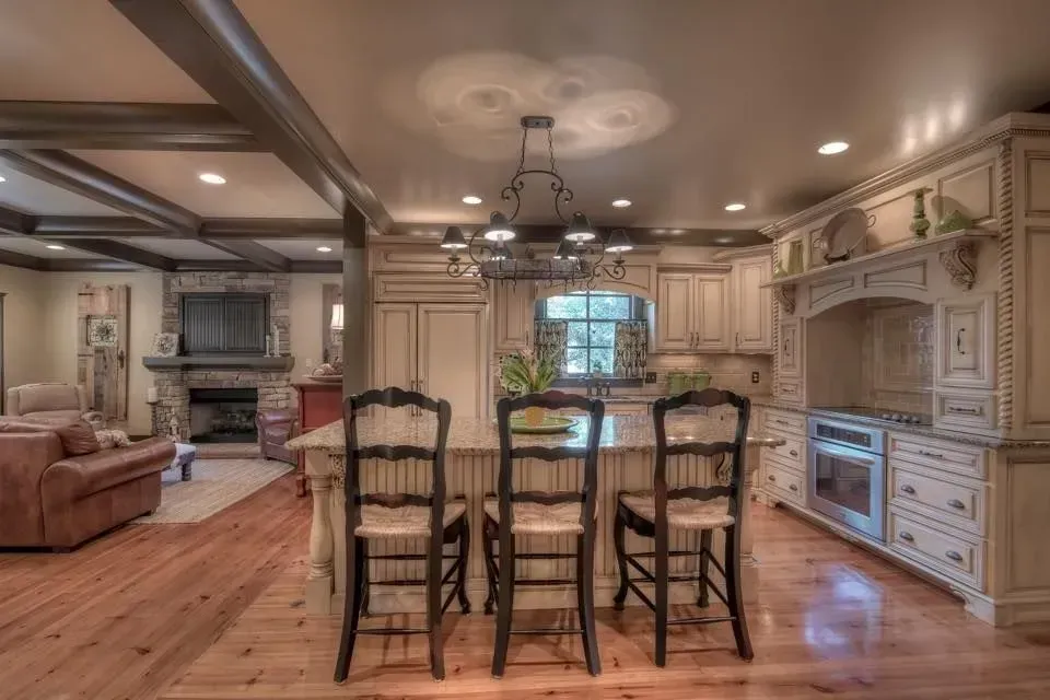 Spacious kitchen with wooden floors, a central island with three chairs, and cream-colored cabinets.