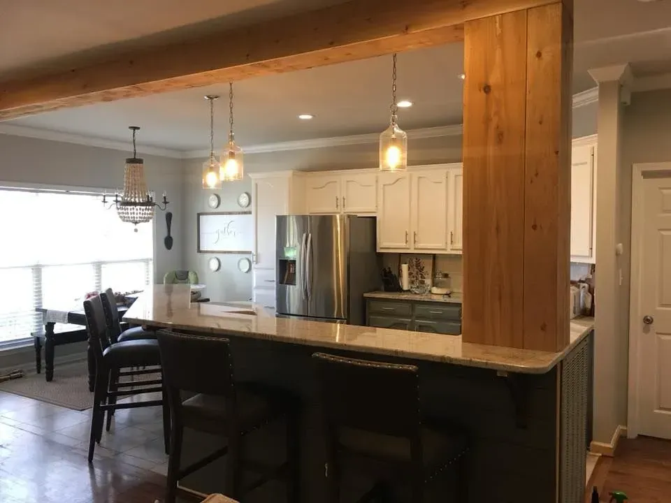 Kitchen with a granite countertop island and overhead wooden beam. Features bar stools, 
