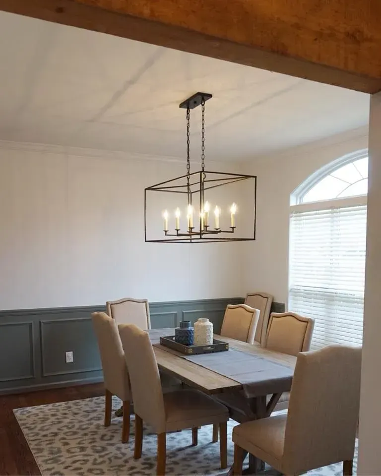 Dining room with a rectangular chandelier over a wooden table and six upholstered chairs. Gray and white color scheme.