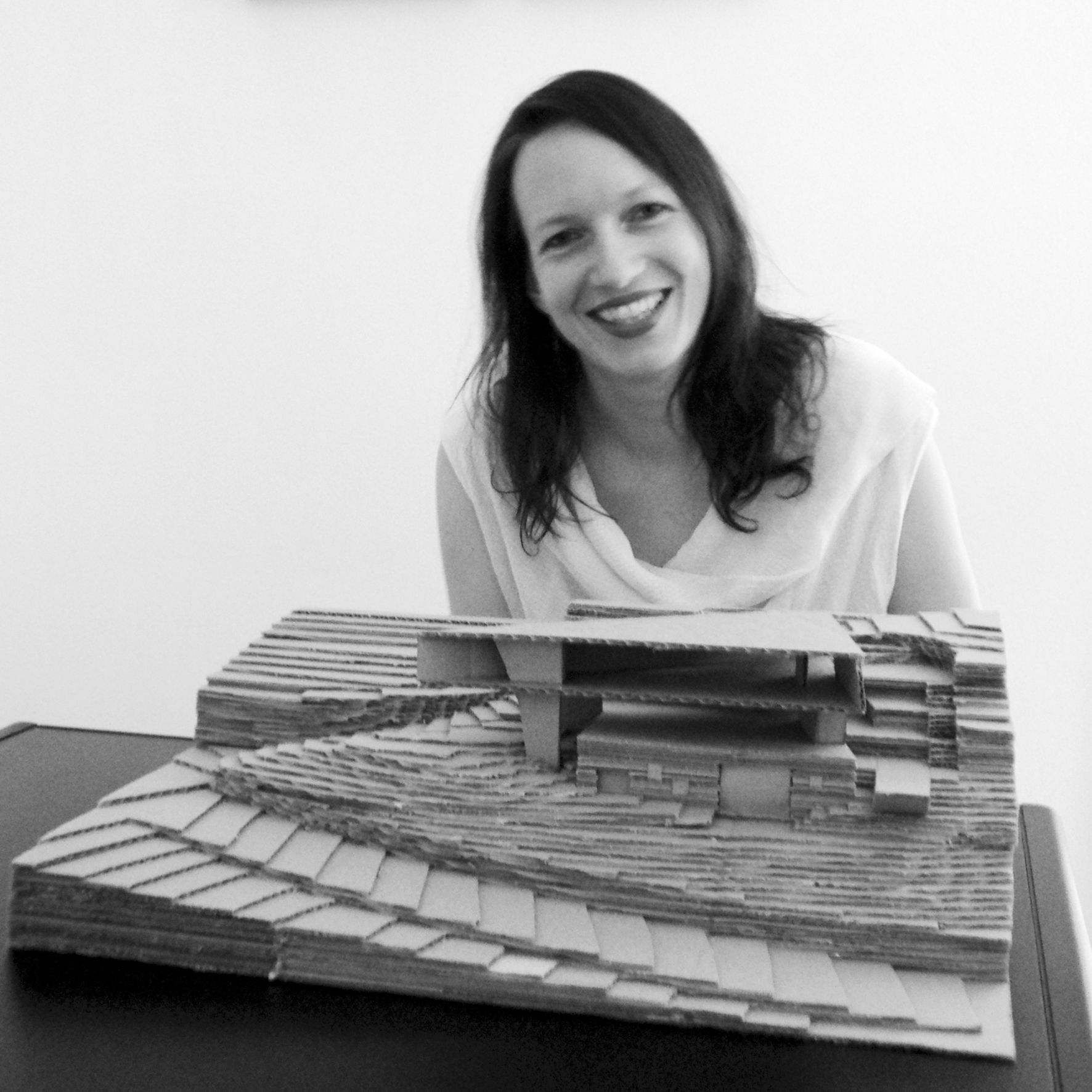 Donna sorridente, china sul modellino di un edificio dal design angolare e stratificato.