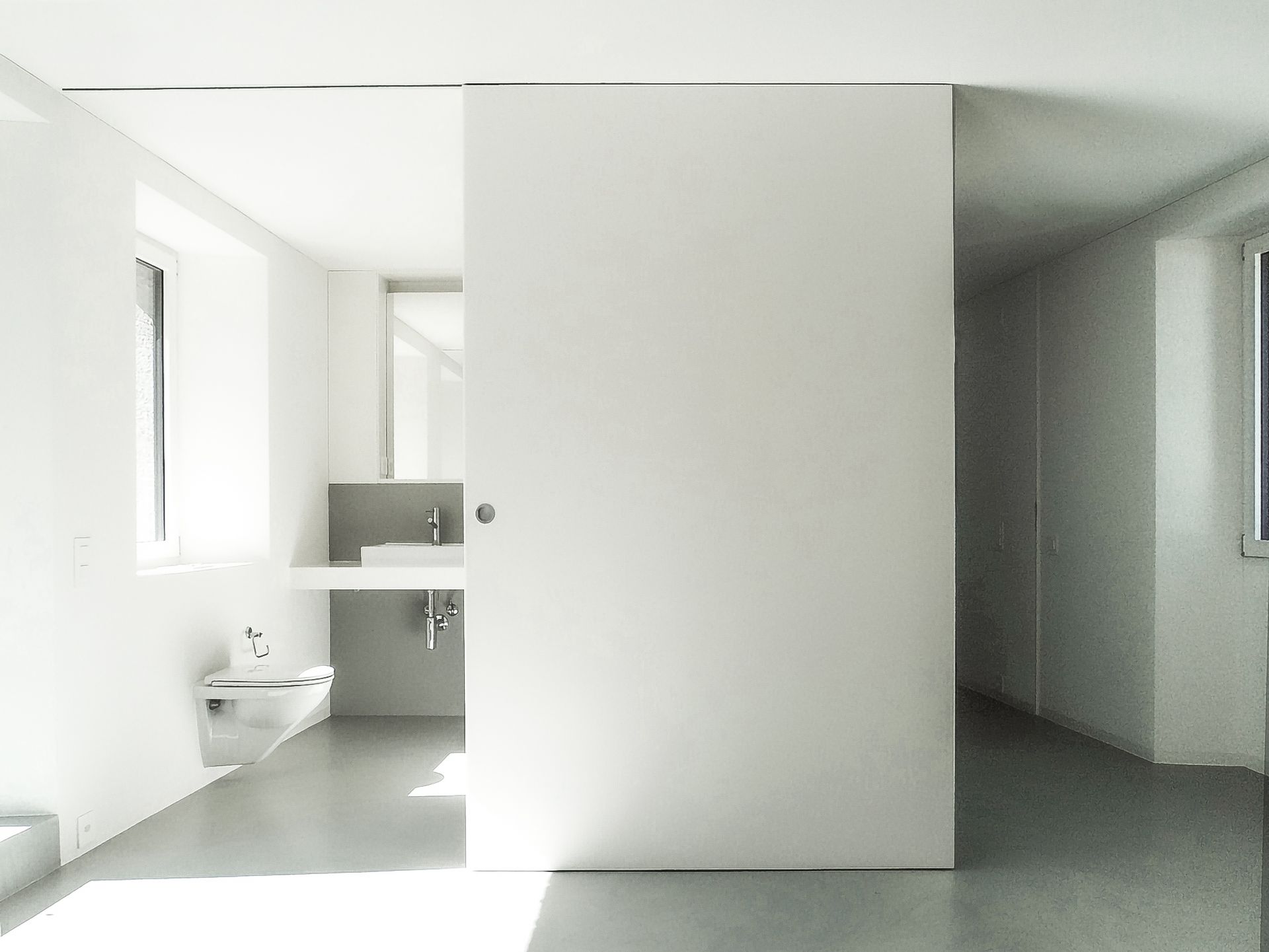 Moderno interno bianco con porta scorrevole aperta che rivela un bagno con lavandino.