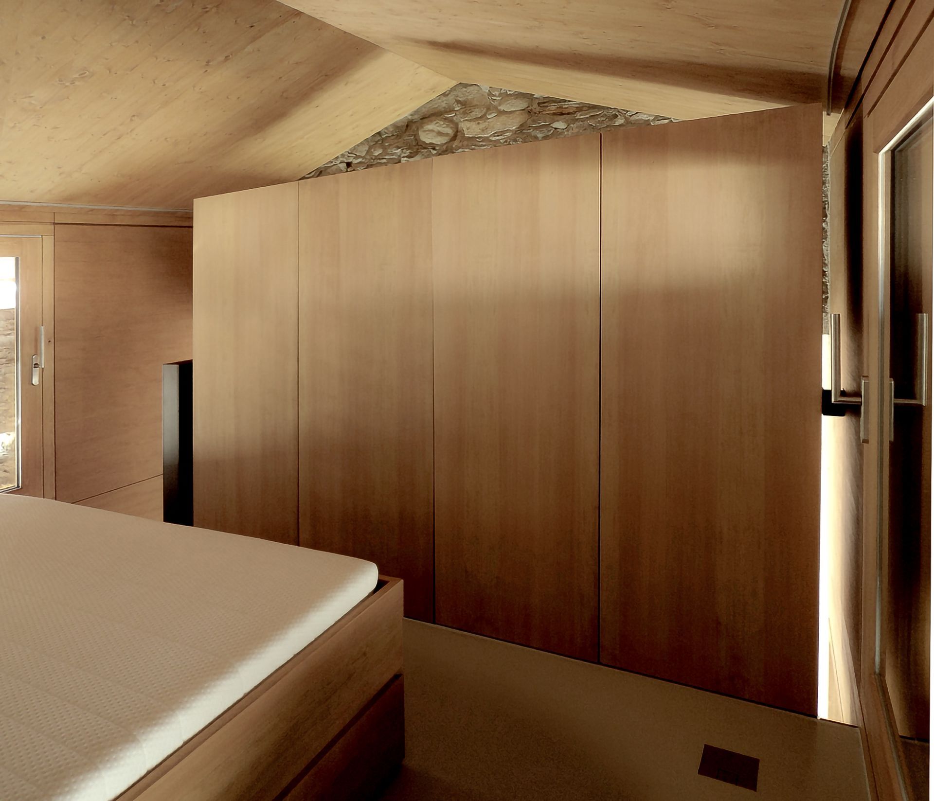 Camera da letto con pareti in legno, letto, grande armadio in legno e dettagli in pietra vicino al soffitto.