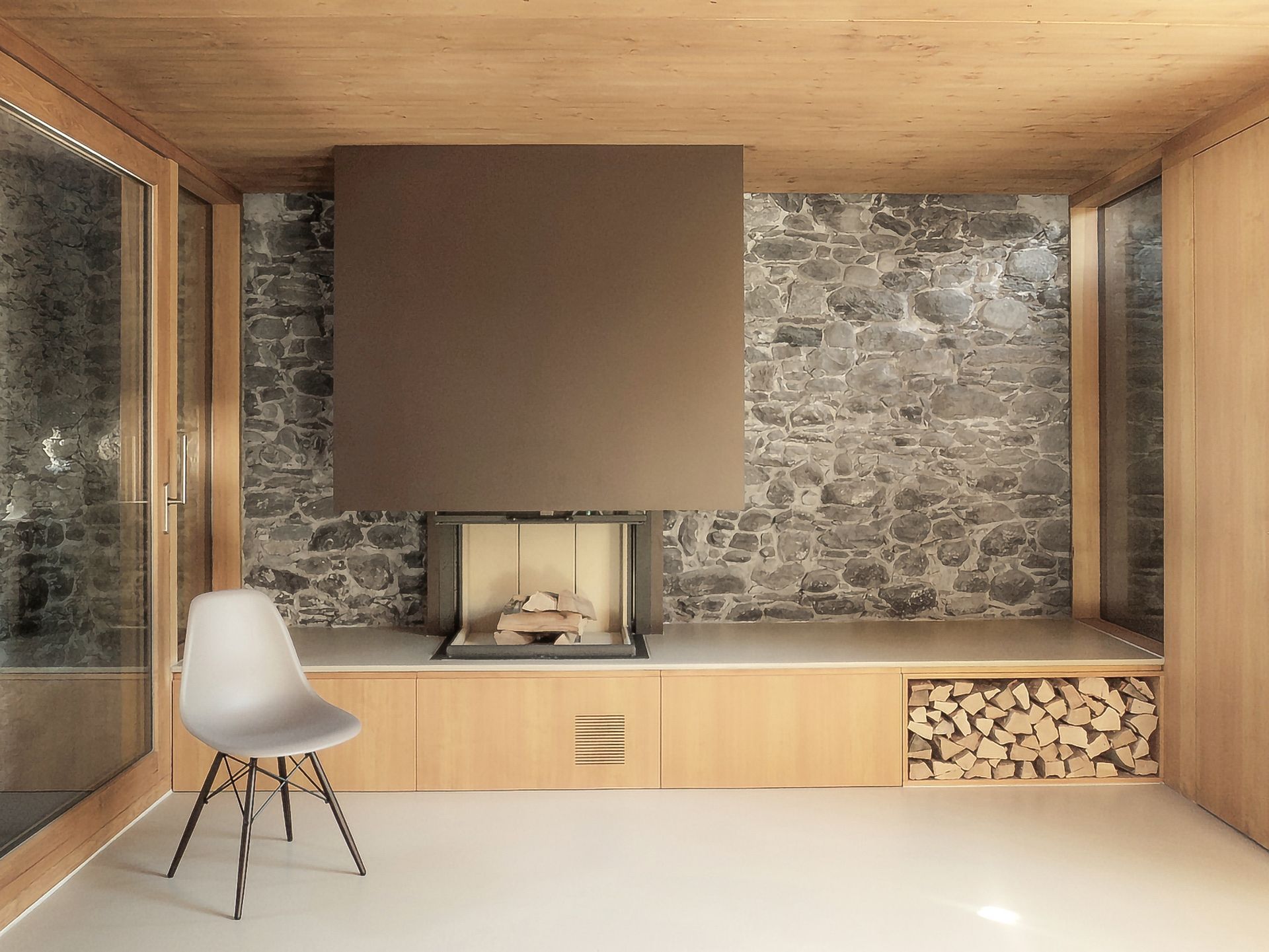 Soggiorno con parete in pietra, camino moderno e pareti e soffitto in legno. Una sedia è posizionata vicino a una finestra.