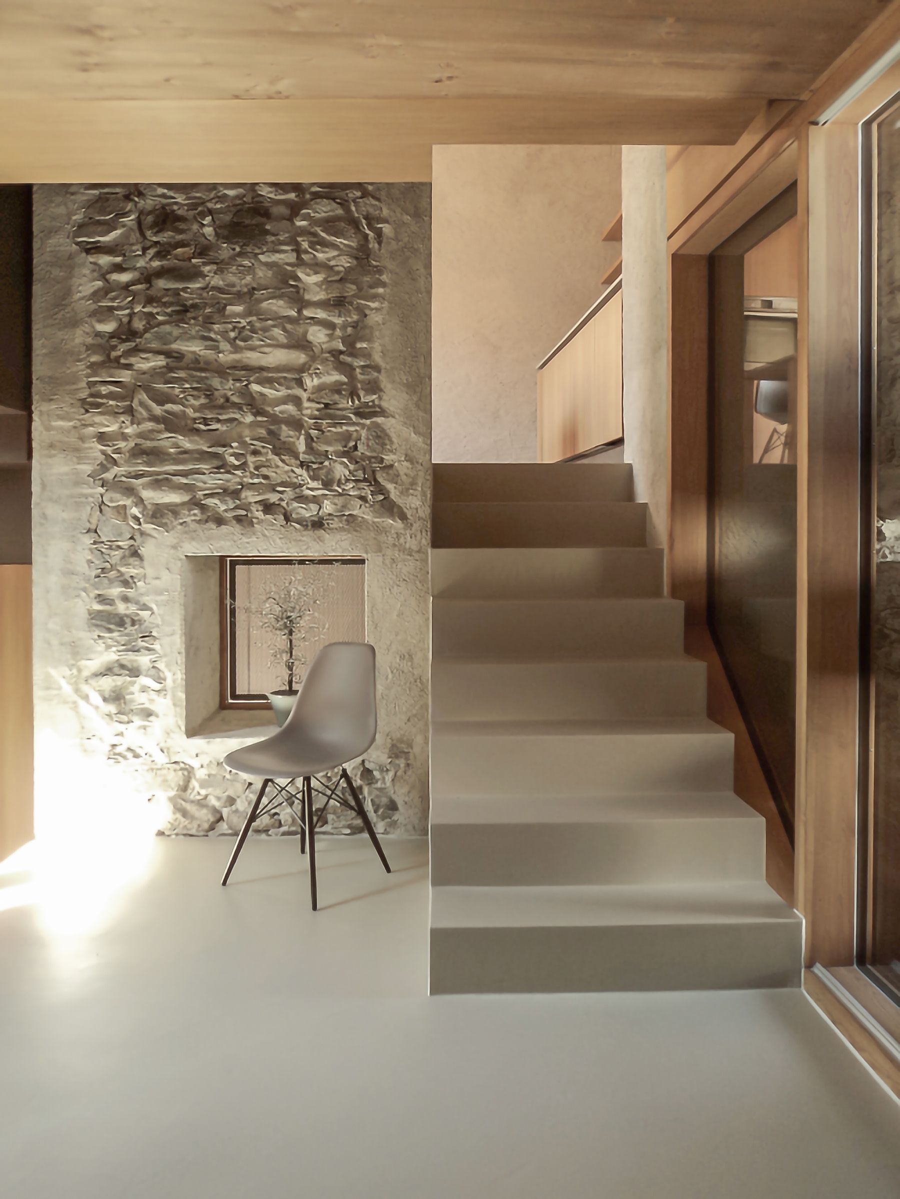 Interno con parete in pietra, scale grigio chiaro, sedia moderna e dettagli in legno.