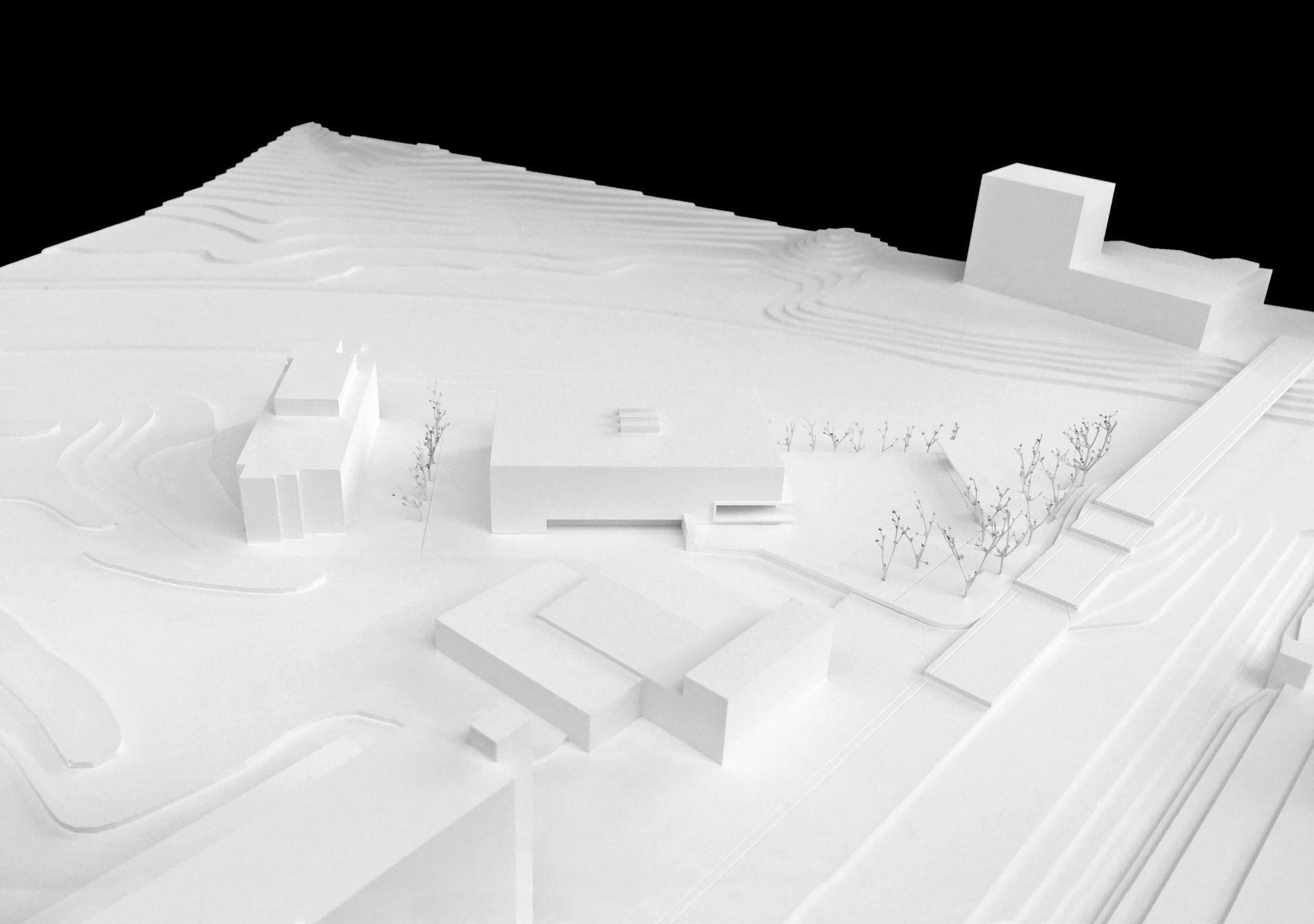 Modello architettonico bianco di un complesso edilizio, con terreno e diverse strutture.