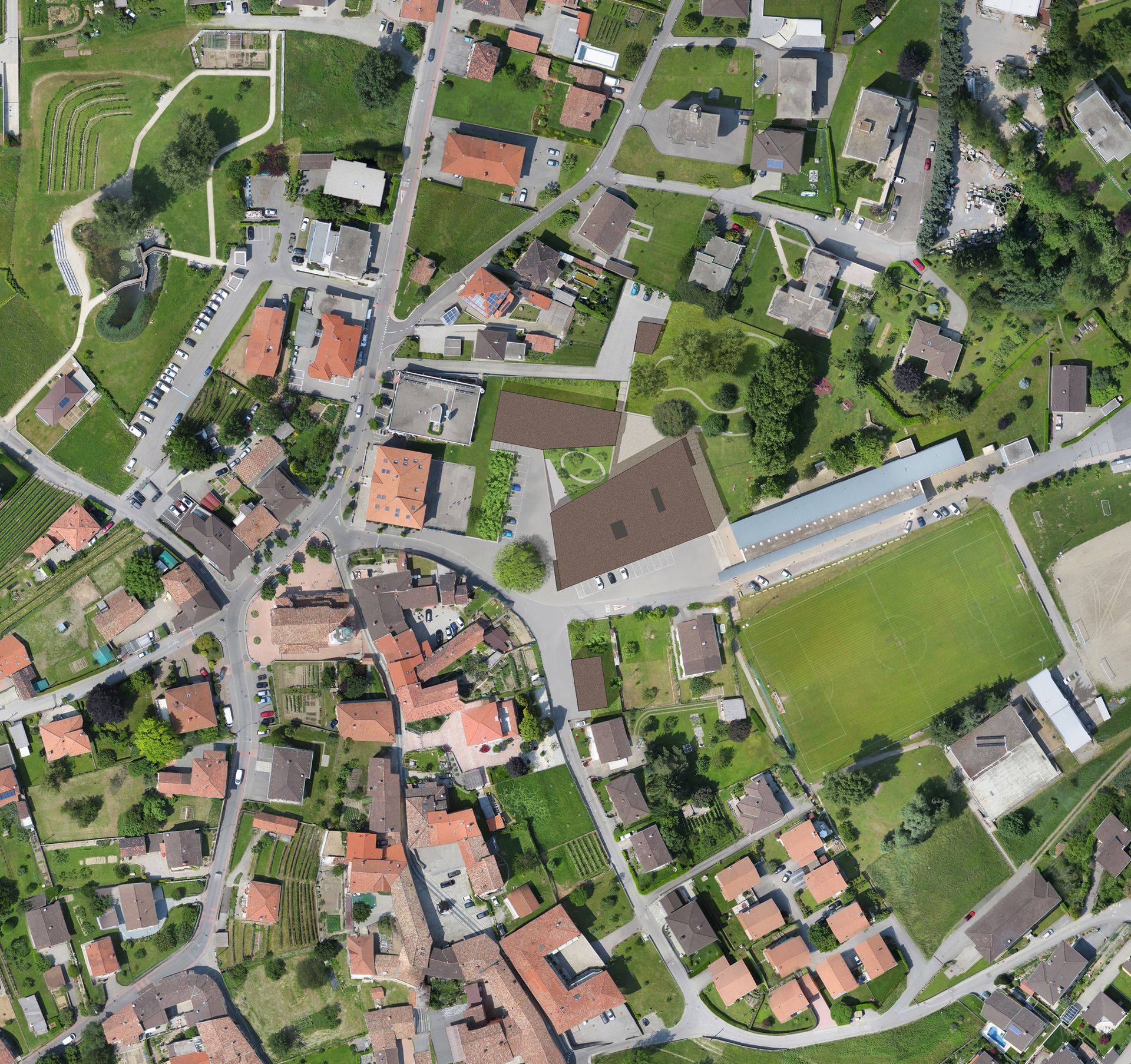 Vista aerea di una città europea con tetti di tegole rosse, edifici, spazi verdi e un tracciato stradale circolare.