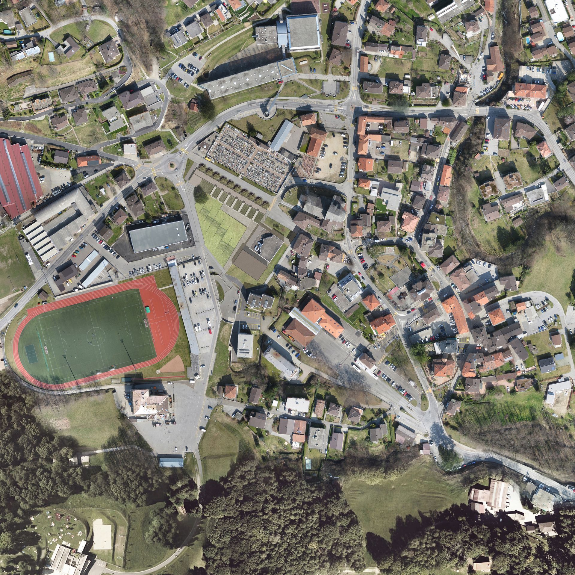 Vista aerea di una città con uno stadio, case, strade e un cimitero.