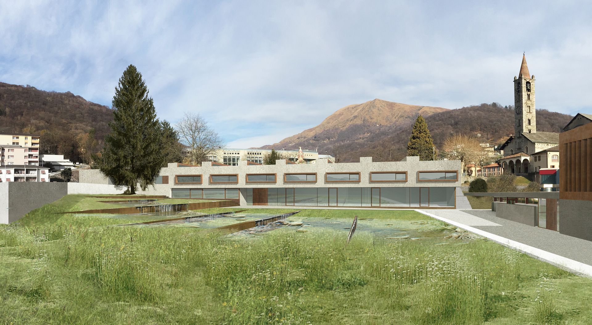 Edificio moderno con finestre rettangolari, prato in primo piano, montagne sullo sfondo, campanile della chiesa visibile.