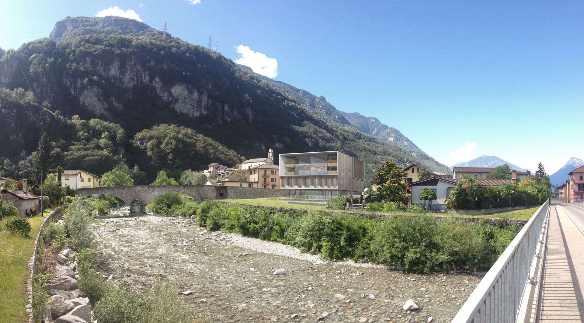 Paesaggio urbano con ponte su un fiume, montagne sullo sfondo sotto un cielo azzurro.