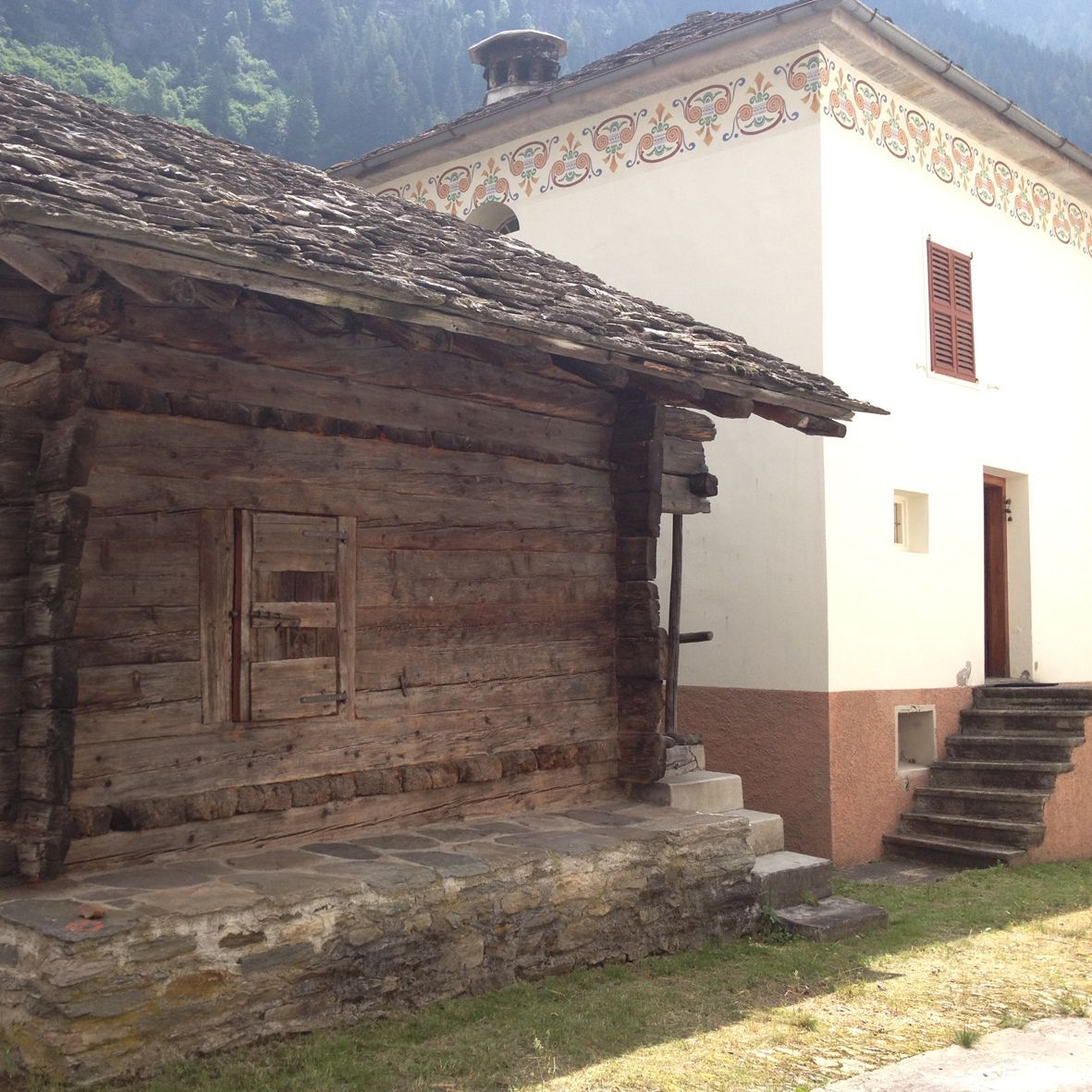 Baita in legno accanto a un edificio bianco con scale in pietra; ambiente rustico.