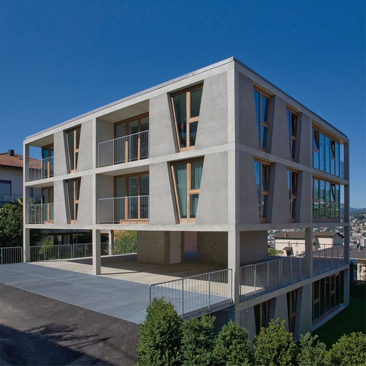 Moderno edificio in cemento con ampie finestre e balconi, sotto un cielo azzurro.