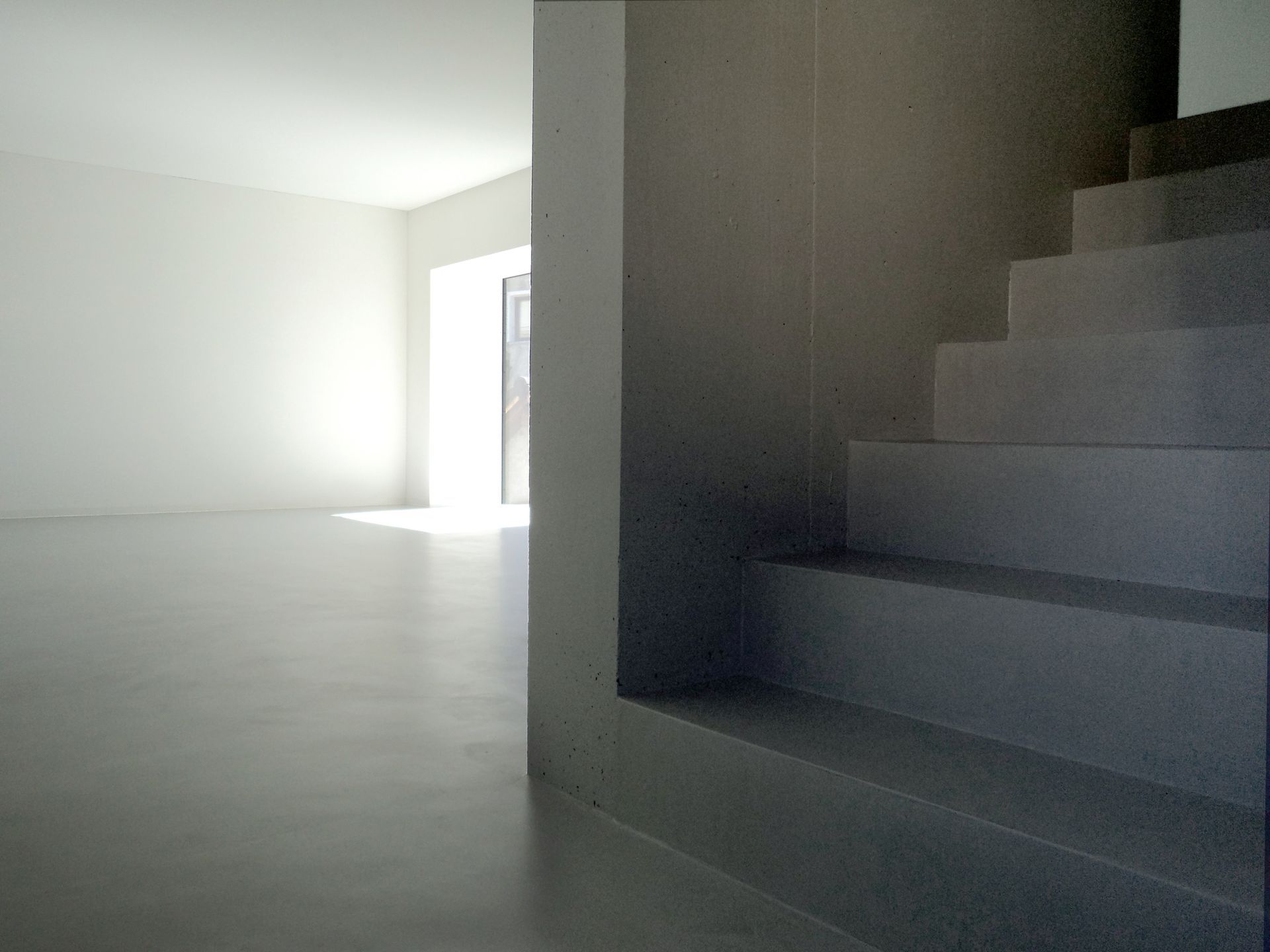 Scala in cemento che sale; sullo sfondo una stanza luminosa e vuota.