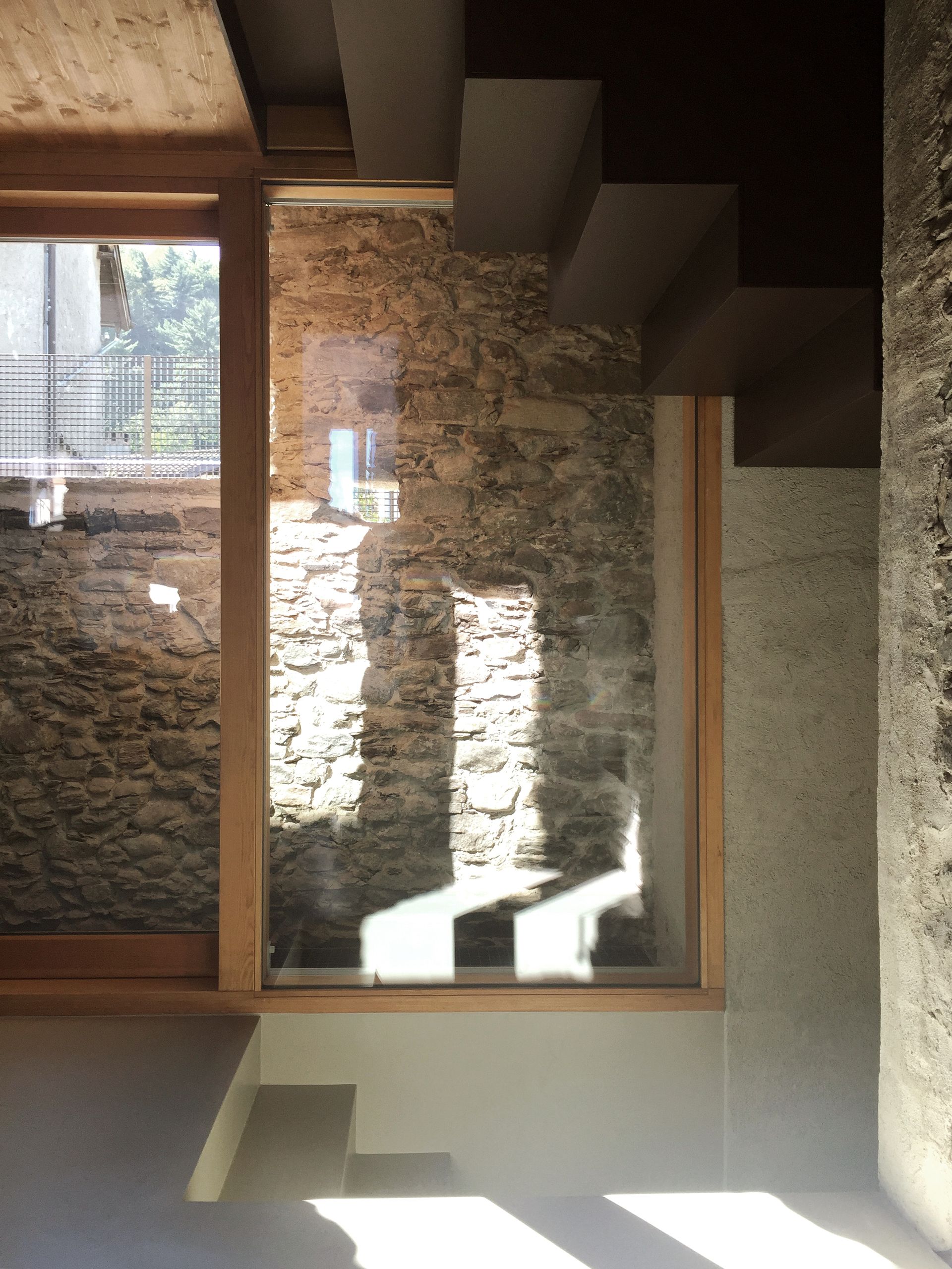 Vista interna di un muro in pietra e scale visibili attraverso le vetrate. La luce del sole crea ombre.