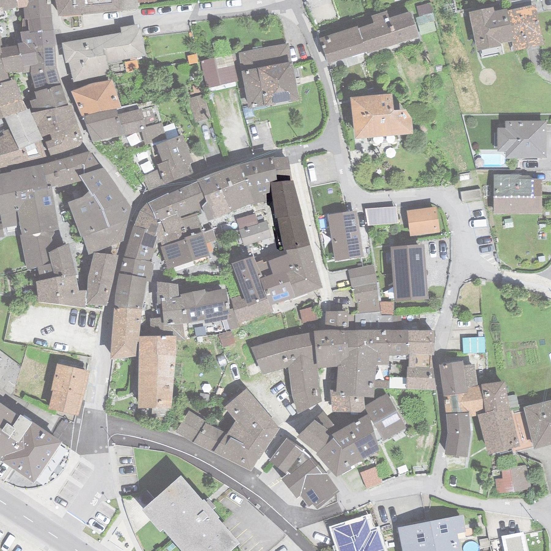 Vista aerea di una città con edifici, strade e spazi verdi. Spiccano diversi edifici dai tetti scuri.