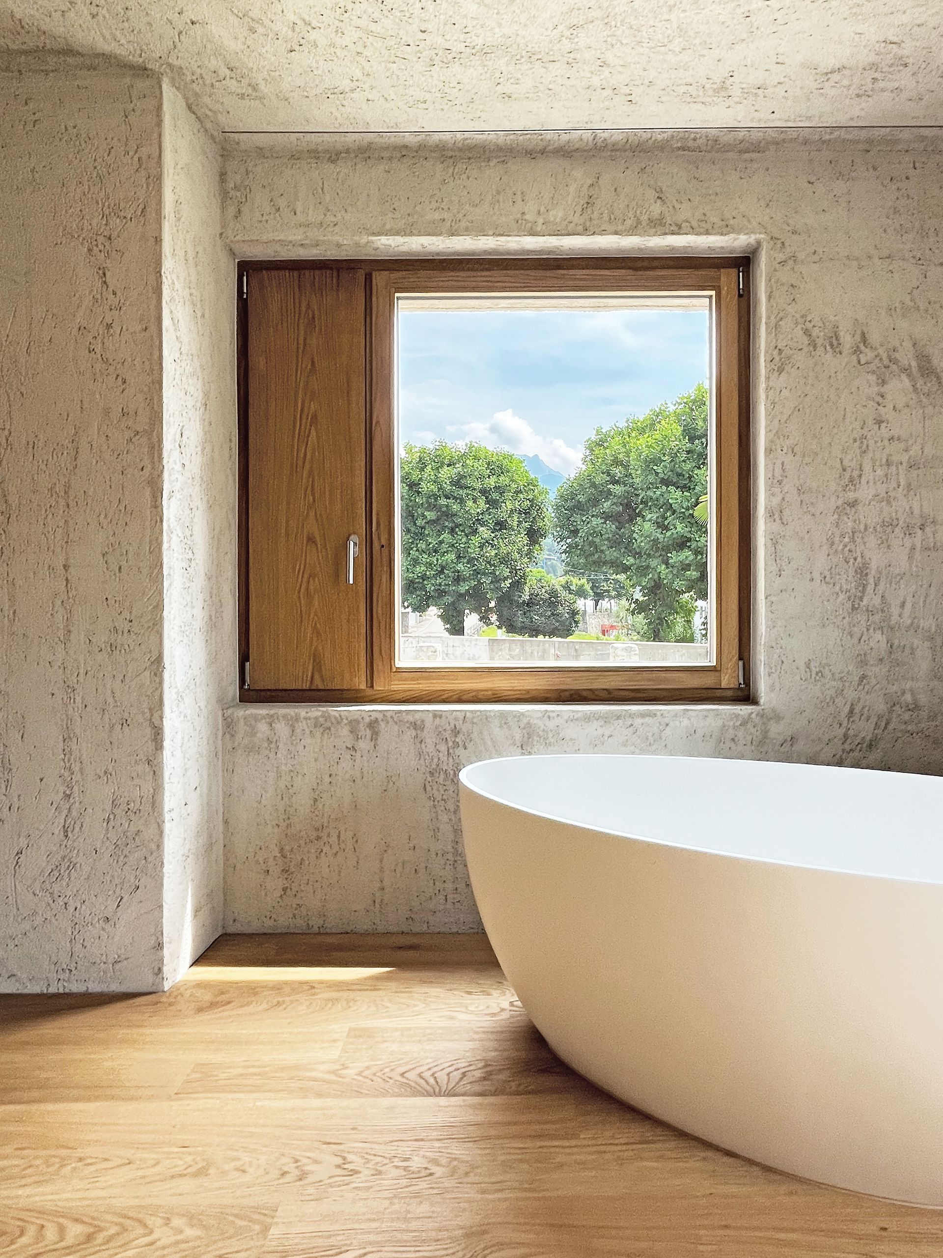 Bagno con vasca moderna, finestra in legno con vista sugli alberi verdi e sulla montagna.