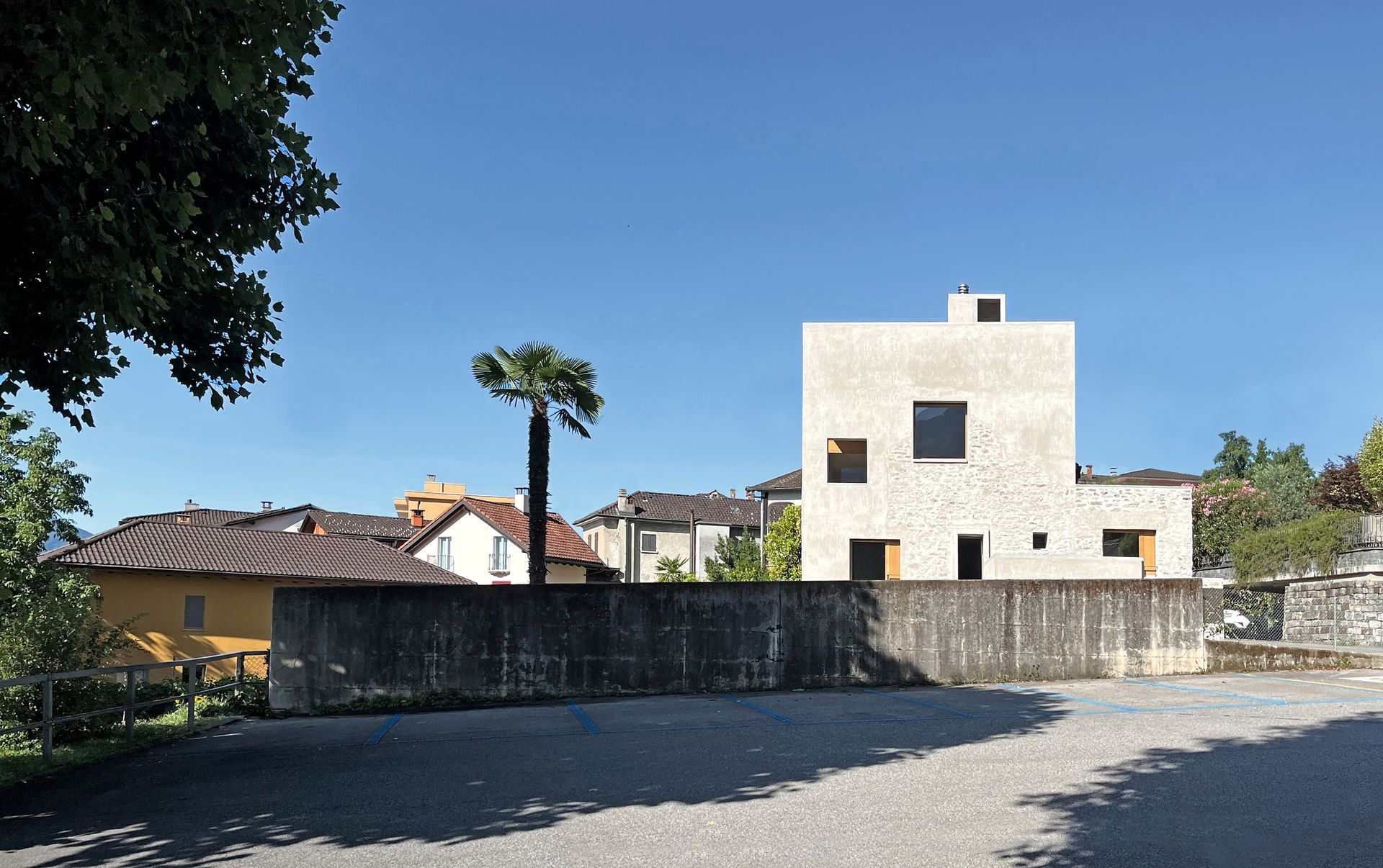 Moderno edificio quadrato con piccole finestre in giornata limpida, dietro un muro di cemento.
