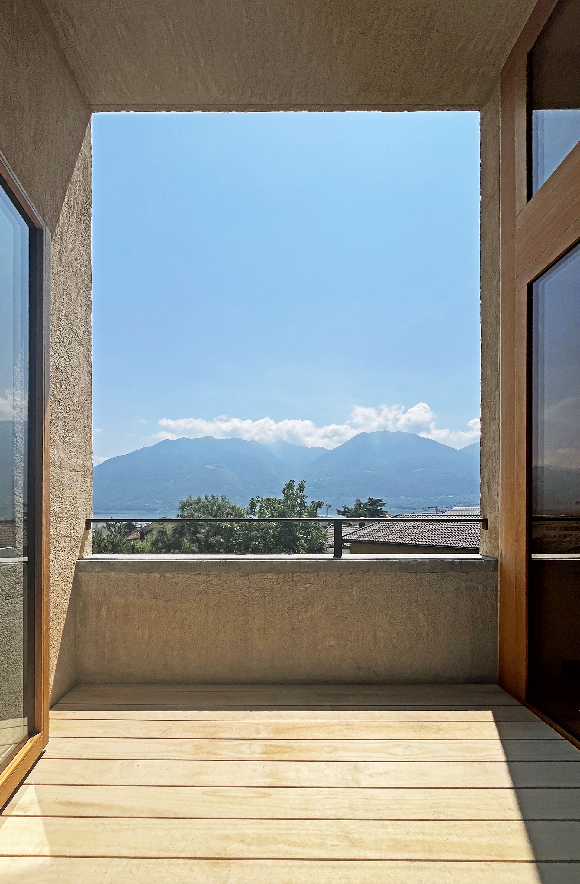 Vista dal balcone: montagne e cielo azzurro attraverso un'apertura rettangolare, porte in legno sui lati.