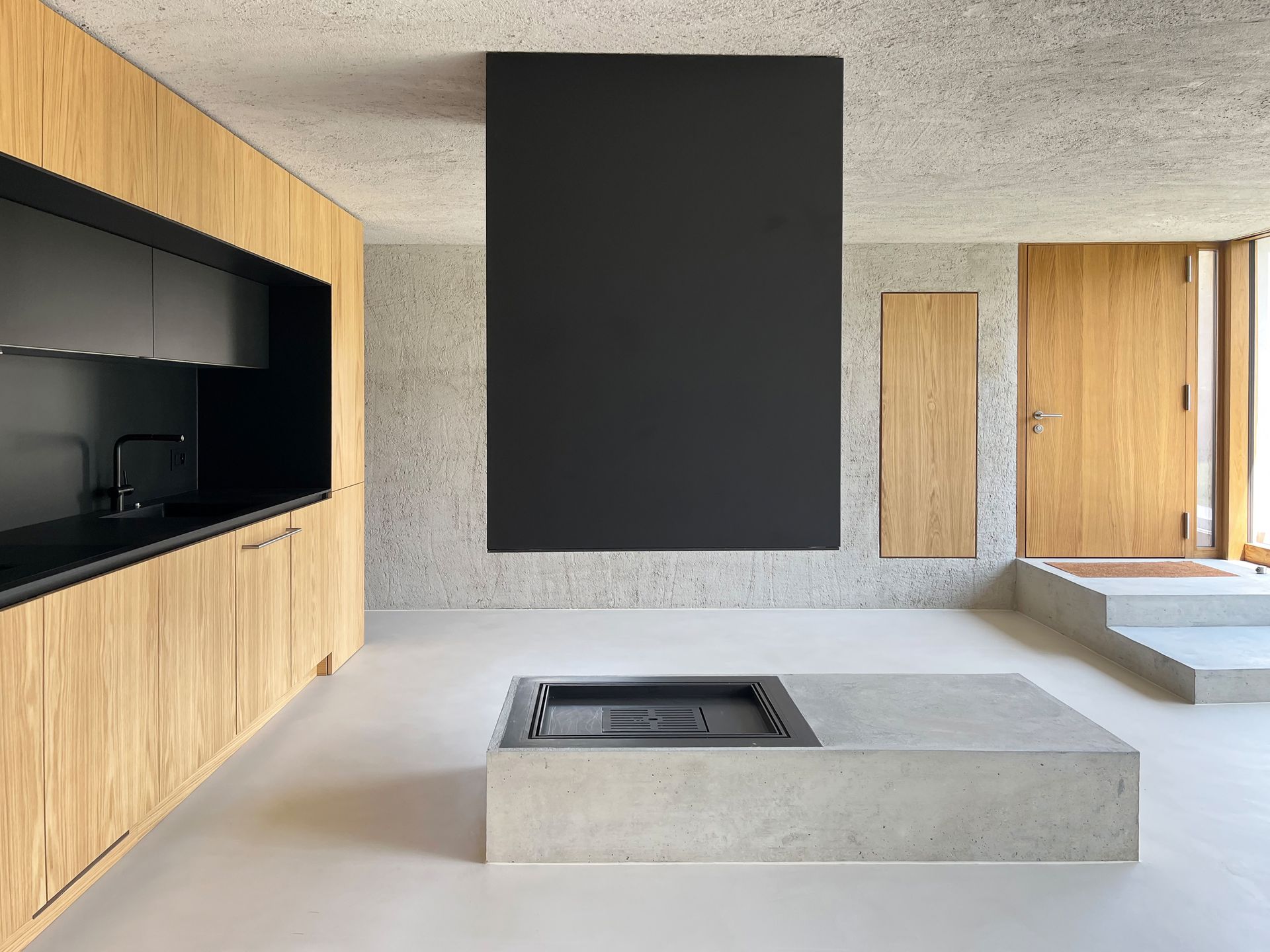 Interni moderni con mobili in legno, pavimento in cemento, camino nero e pareti con macchie chiare.