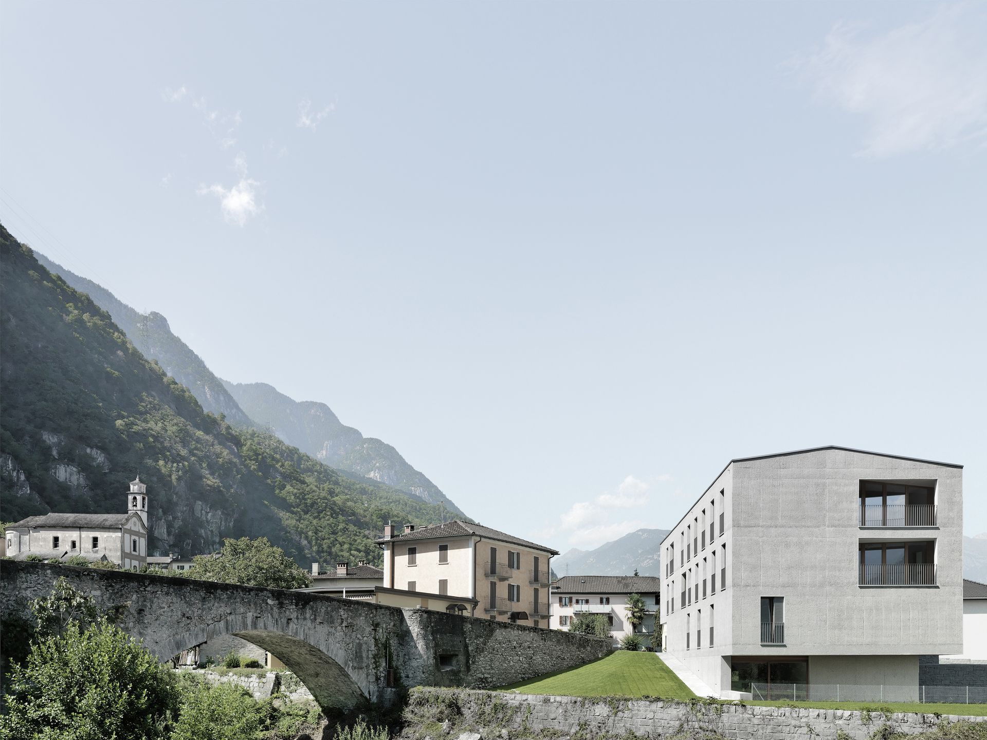 Un edificio moderno accanto a un vecchio ponte e a un villaggio con le montagne sullo sfondo.