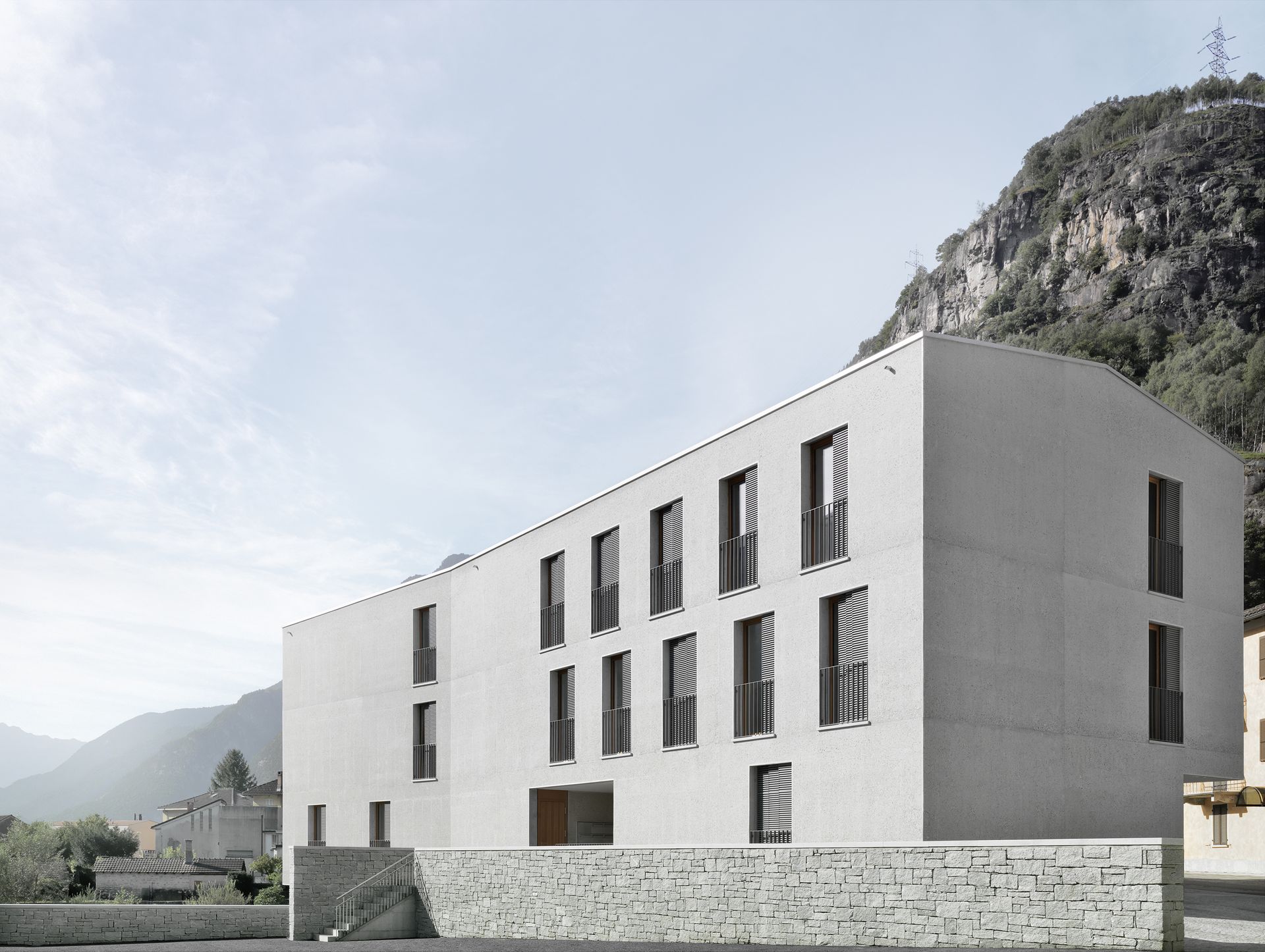 Un edificio rettangolare, di colore chiaro, con finestre scure e strette, incastonato in un paesaggio montuoso.