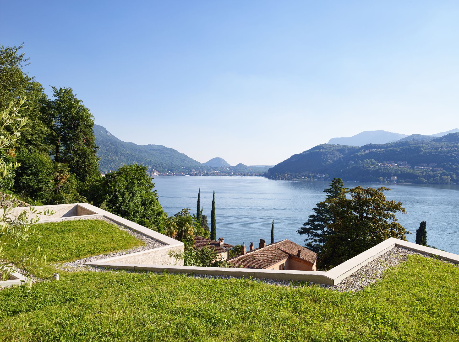 Lussureggiante giardino verde a più livelli con vista sul lago e sulle montagne sotto un cielo azzurro.