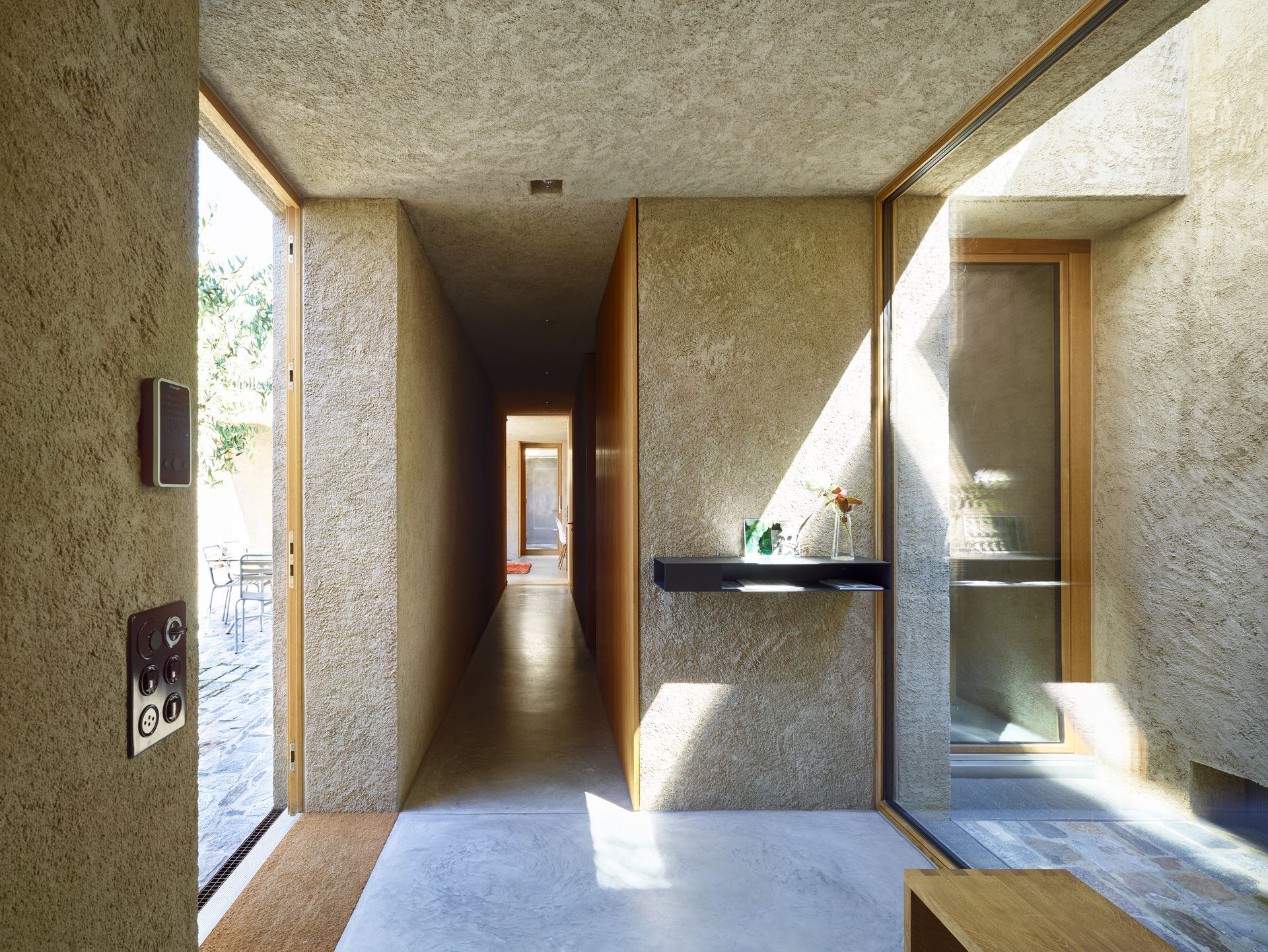 Corridoio interno con pareti strutturate, luce naturale. Porta aperta sulla sinistra, porta in legno di fronte.