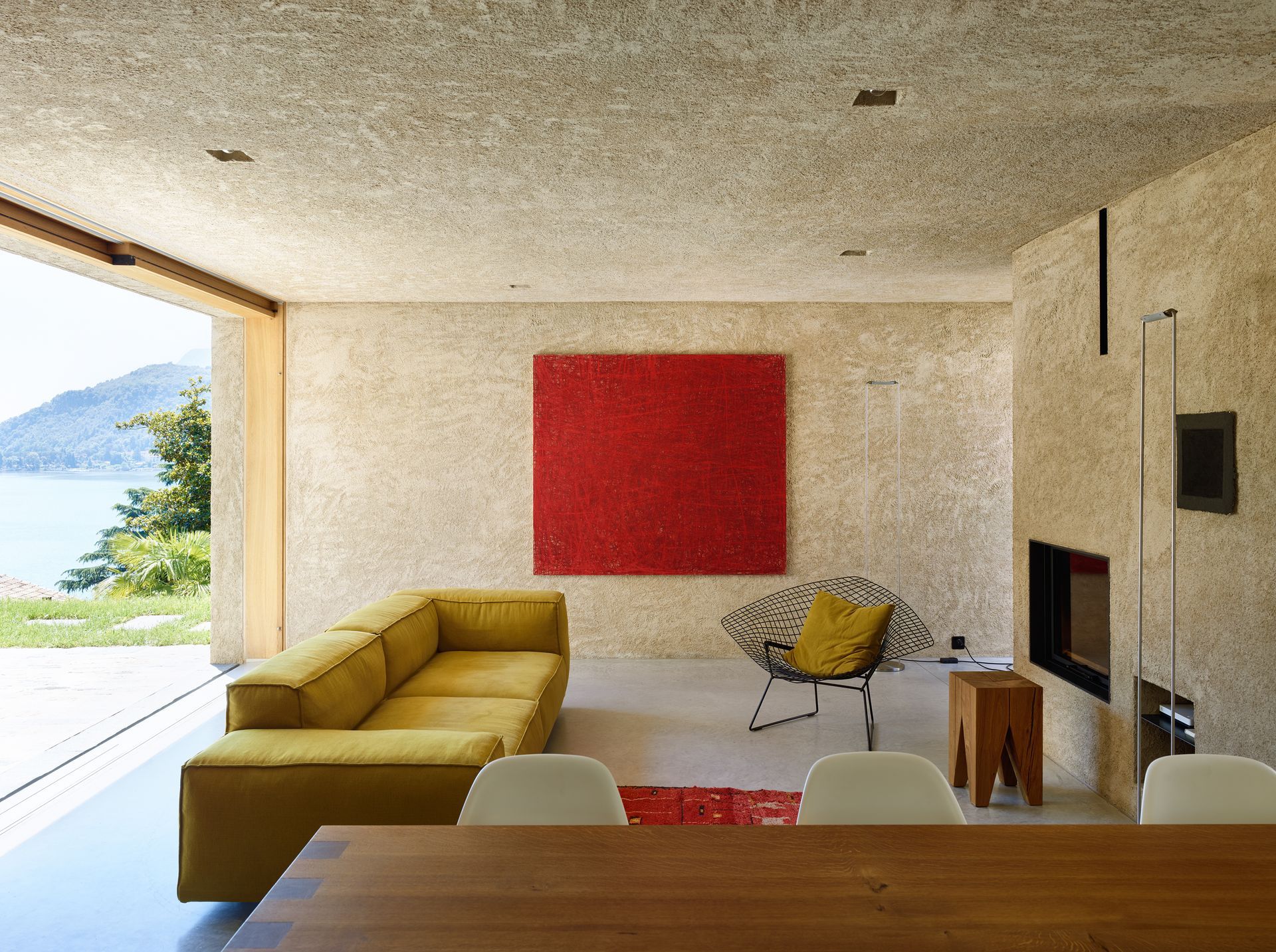 Soggiorno moderno con divano giallo, opere d'arte rosse, camino e vista aperta sull'acqua.