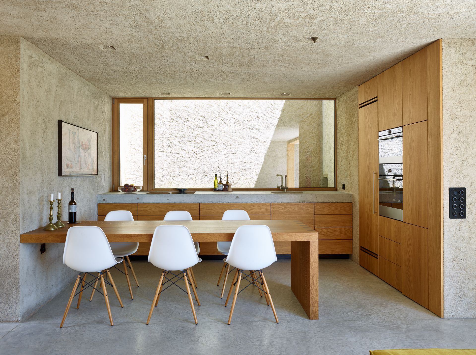 Sala da pranzo con tavolo in legno e sedie bianche, mobili in legno a muro e pareti strutturate.
