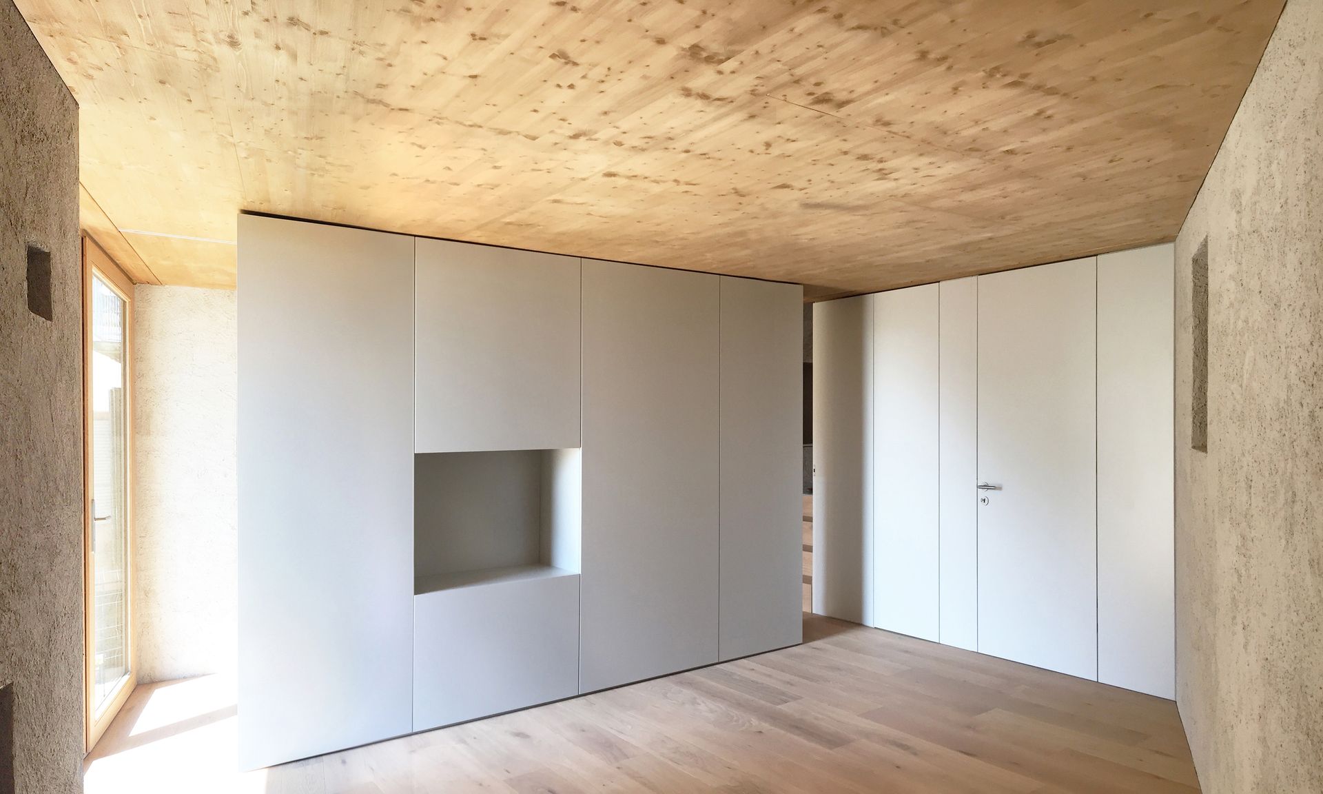 Stanza interna con pareti, soffitto e pavimento in legno chiaro. Mobili bianchi a muro con zona incassata.