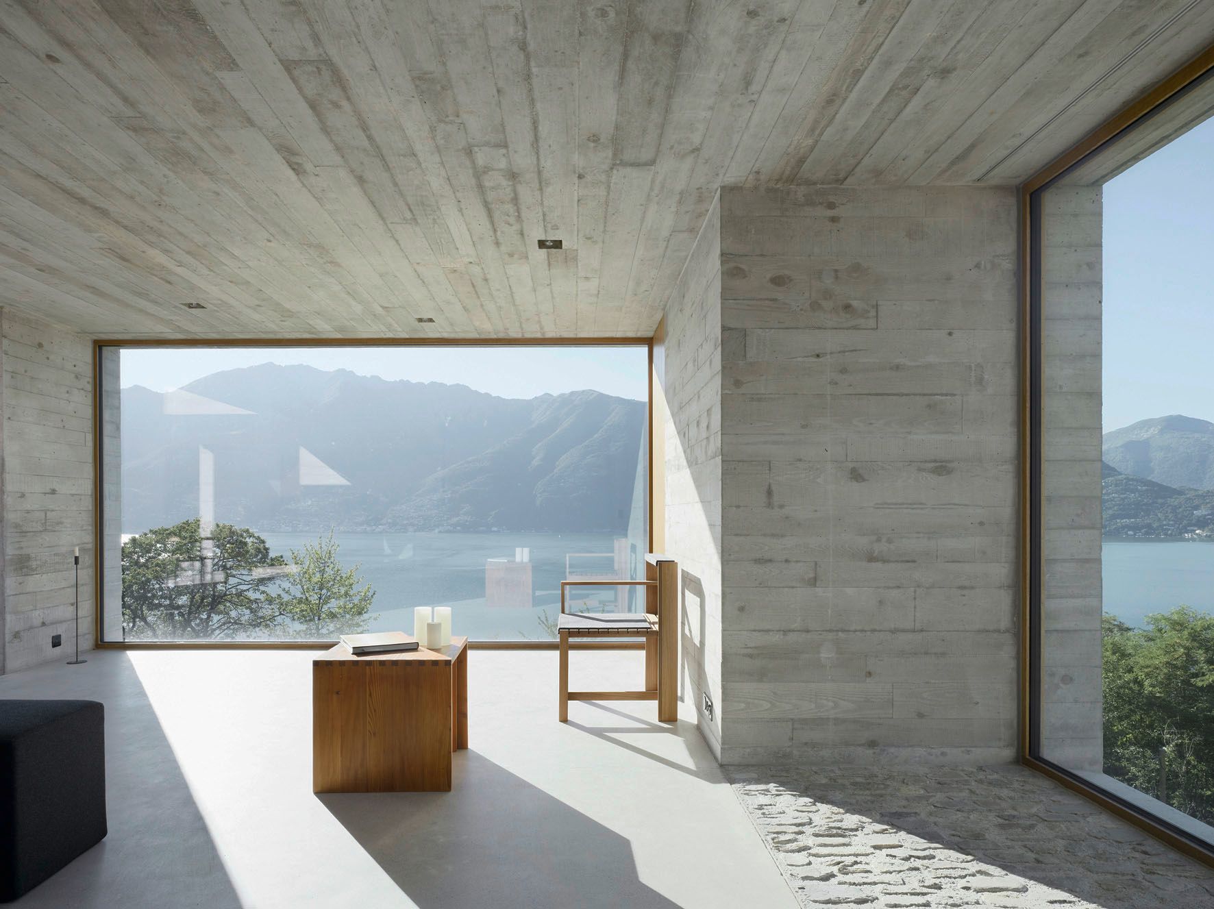 Interni moderni con ampie finestre con vista sul lago e sulle montagne. Pareti in cemento, mobili in legno, luce naturale.