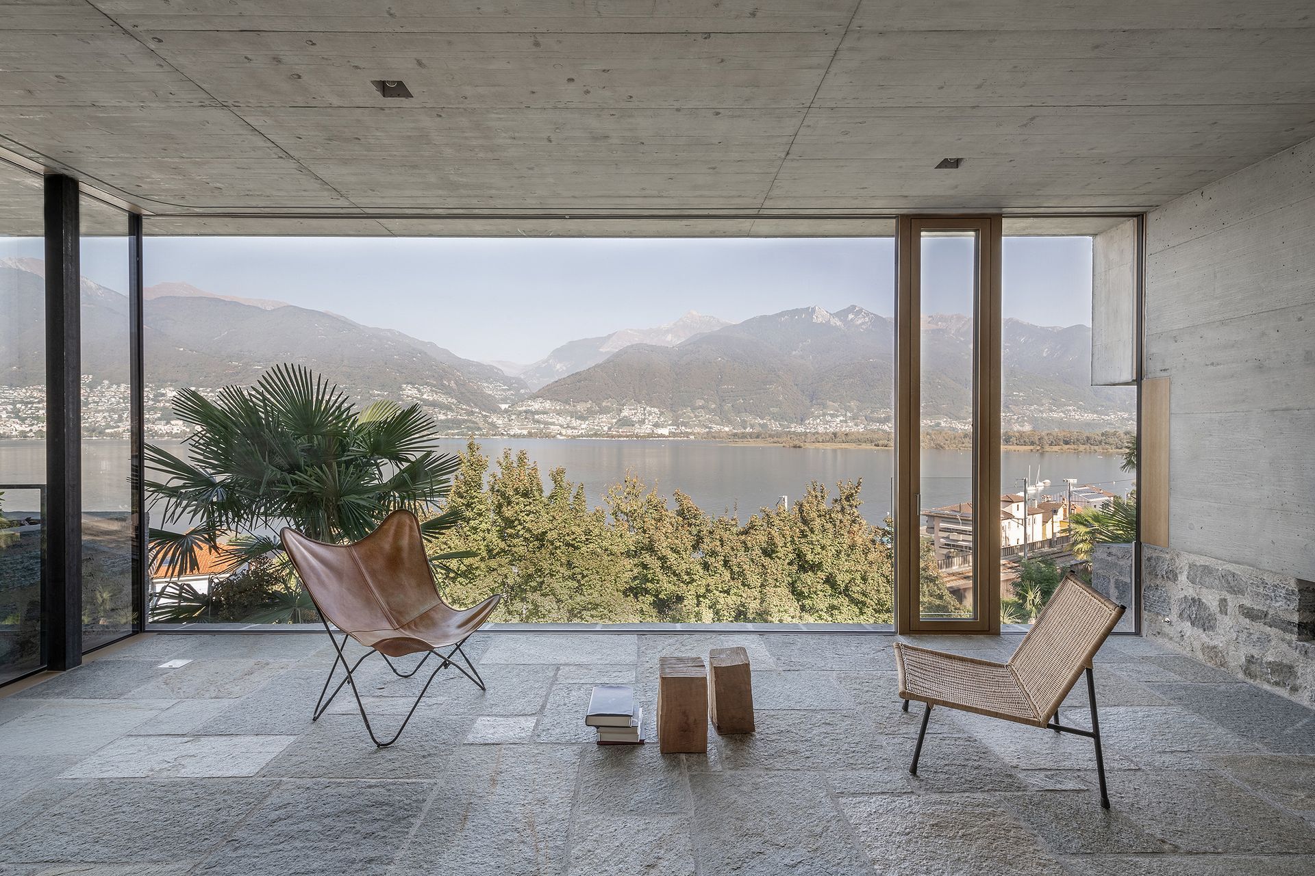 Uno spazio abitativo moderno all'aperto con vista sulle montagne e sul lago, arredato con due sedie e un tavolino.