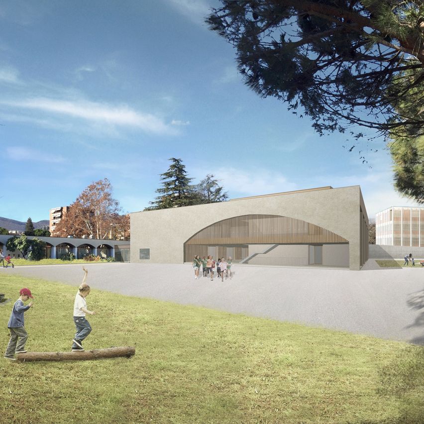 Bambini che giocano su un campo erboso di fronte a un moderno edificio scolastico con un ingresso ad arco in legno.