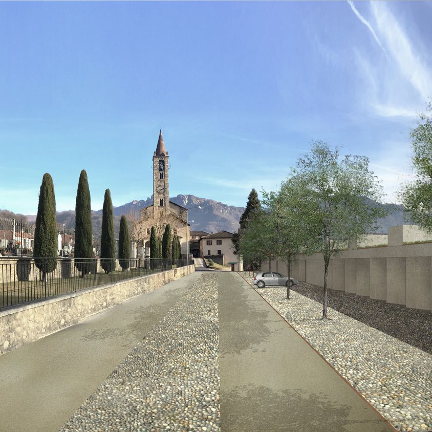 Strada acciottolata con chiesa e montagne sullo sfondo sotto un cielo azzurro.