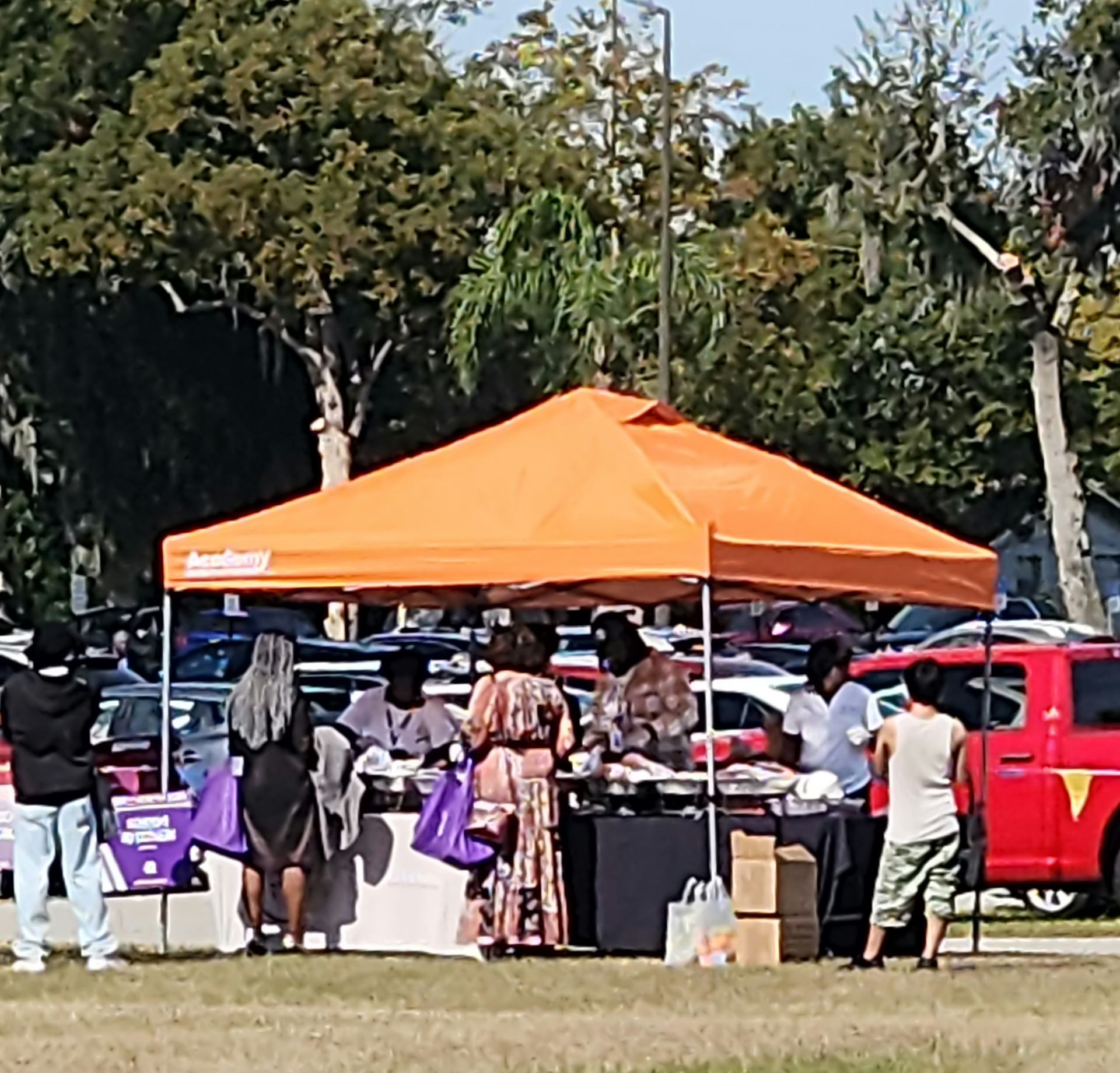 Orange tent with people at tables, outdoors; cars and trees in the background.