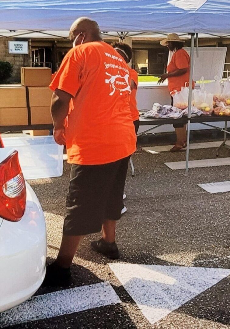 Person in orange shirt near a food distribution tent. Others in orange shirts are serving food.